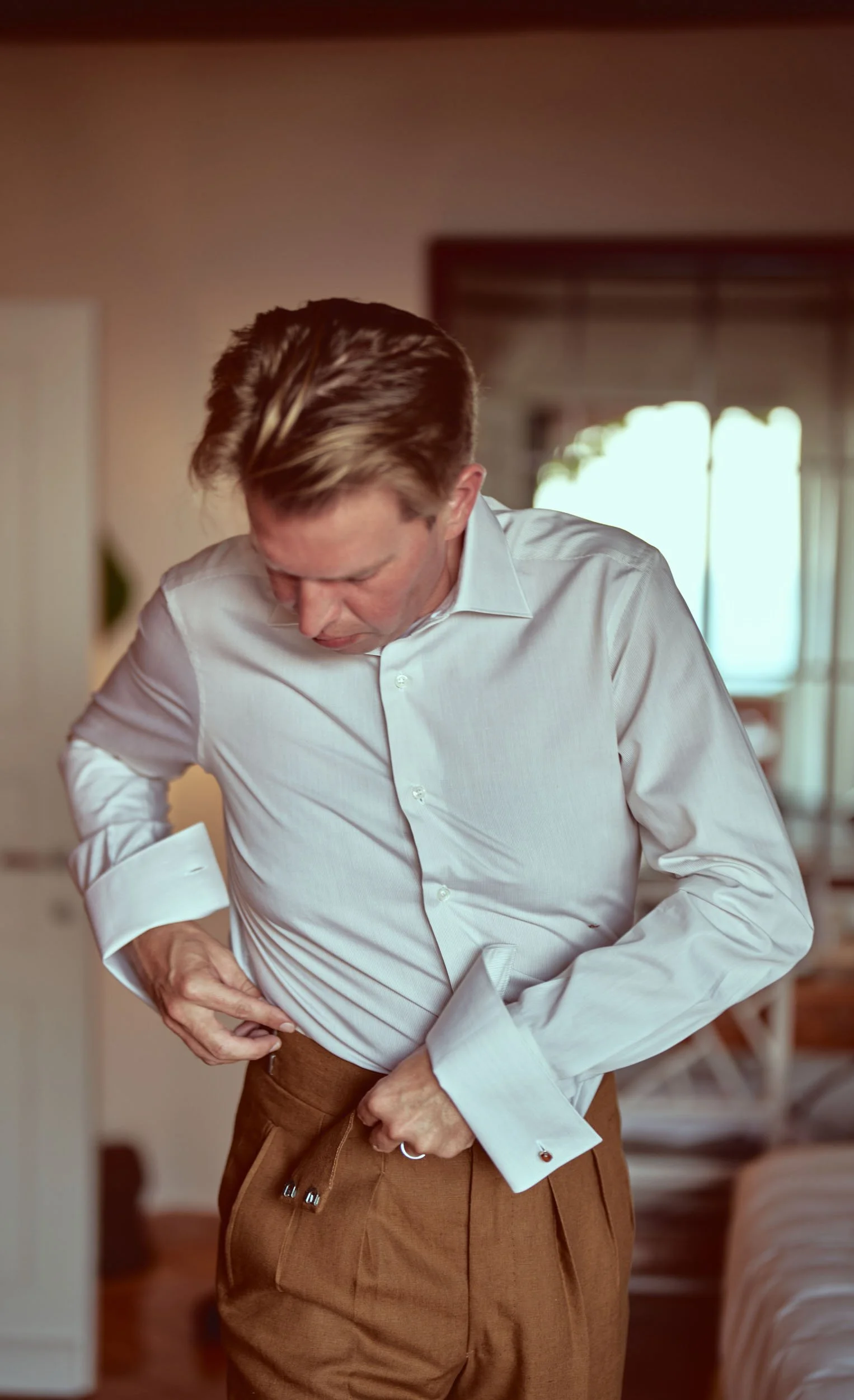 Groom getting ready, adjusting pleated trousers.