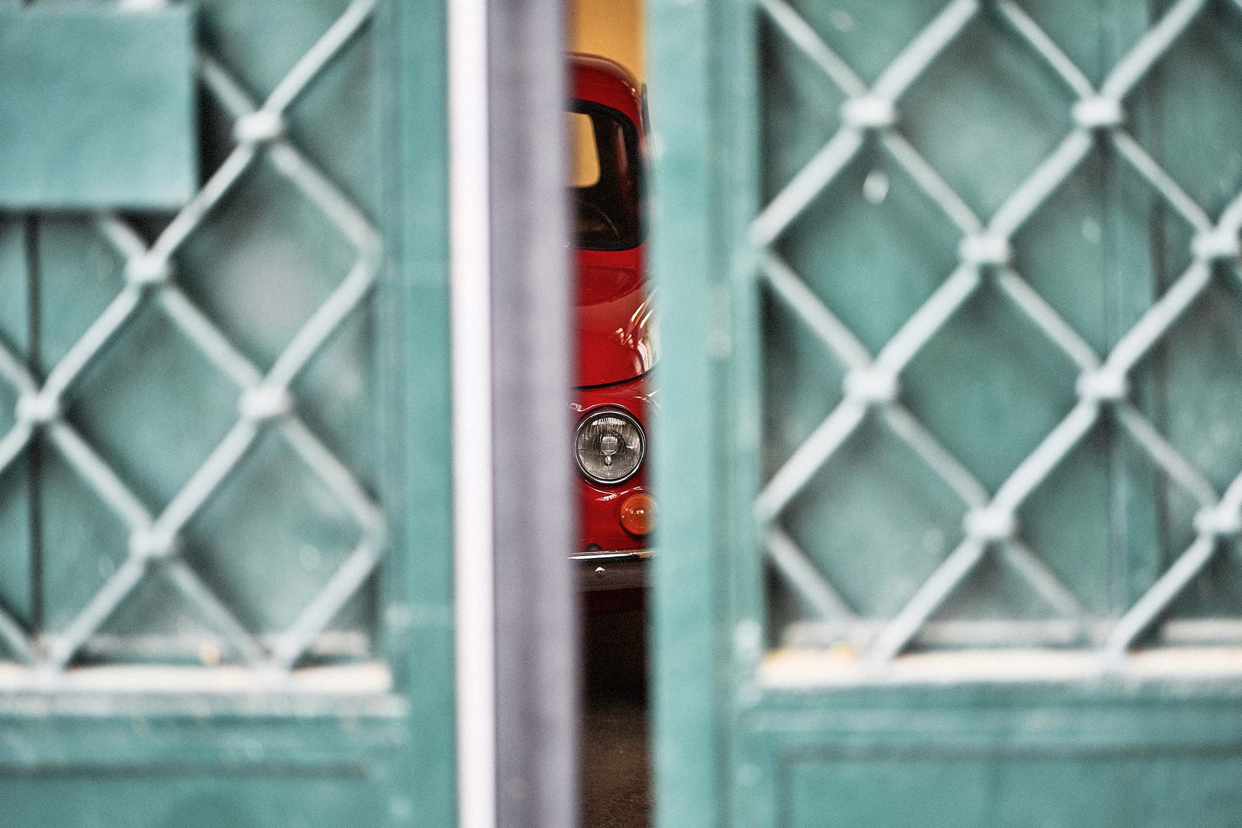 Iconic red Fiat 500 seen through a green gate in Rome. Italian lifestyle inspiration for destination weddings.