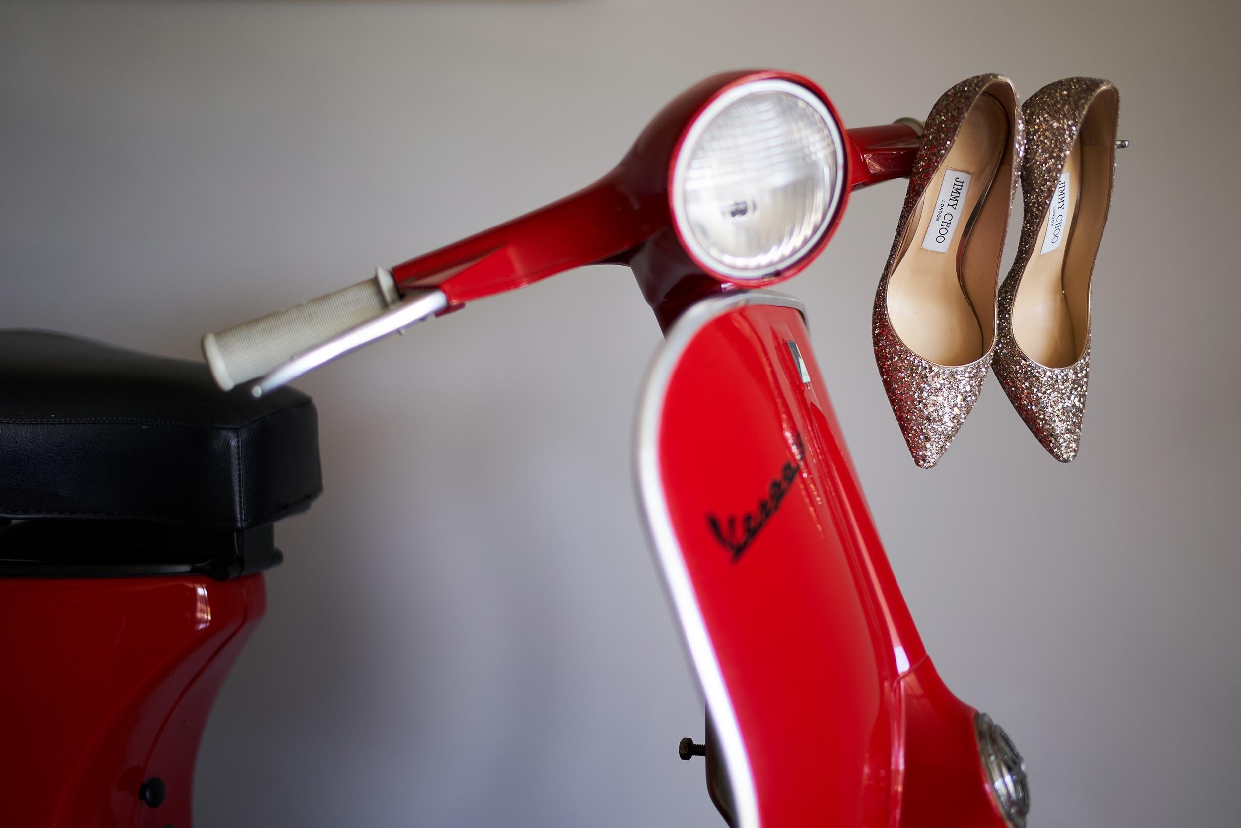 A touch of irony: Red Vespa with Jimmy Choo sparkly heels hanging from the handlebars. Editorial wedding photography at Resort Colonna capturing the Italian Dolce Vita vibe.
