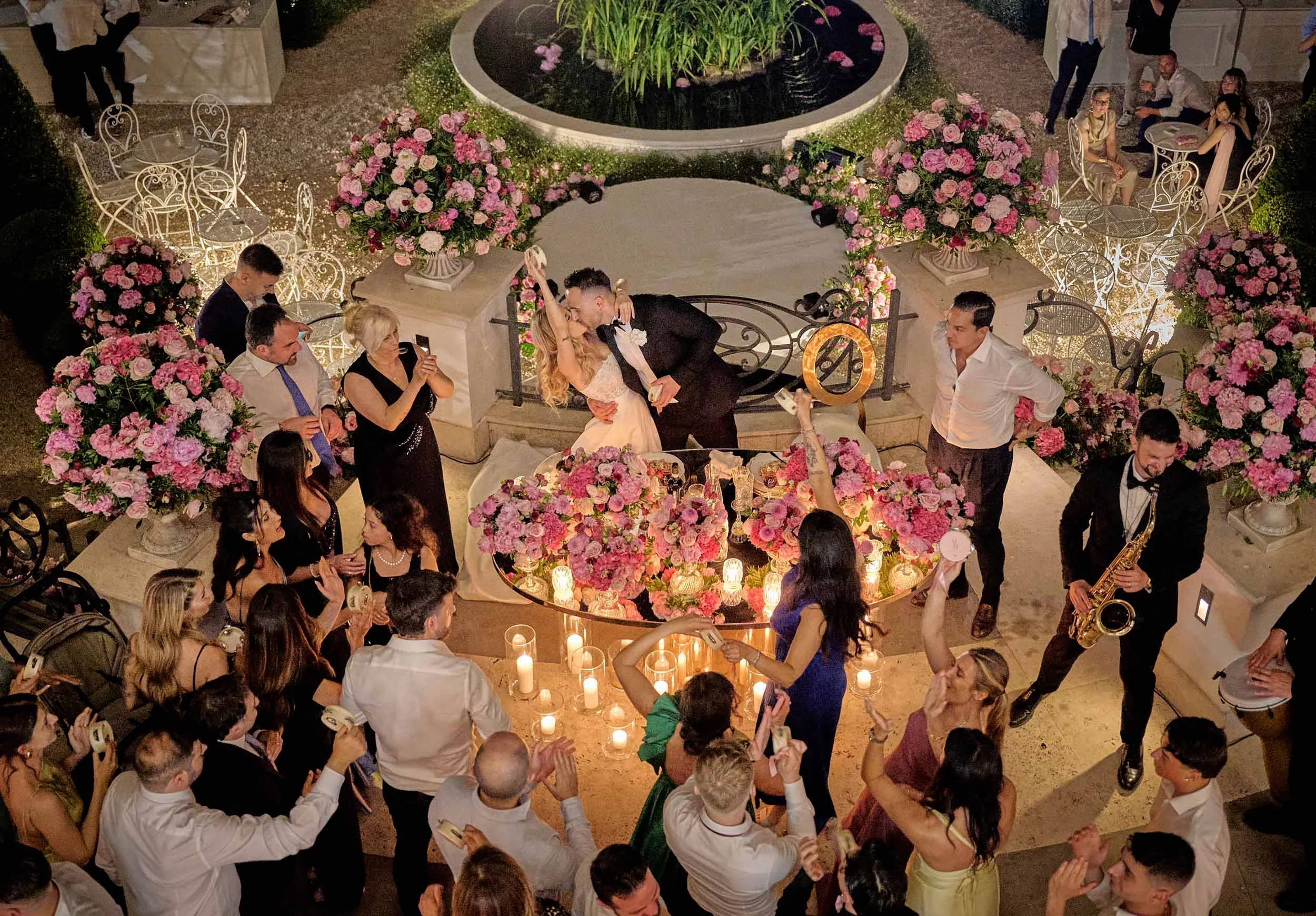 Top-down view of the bride and groom kissing during the wedding reception surrounded by guests and music, dynamic and authentic party reportage in Rome.