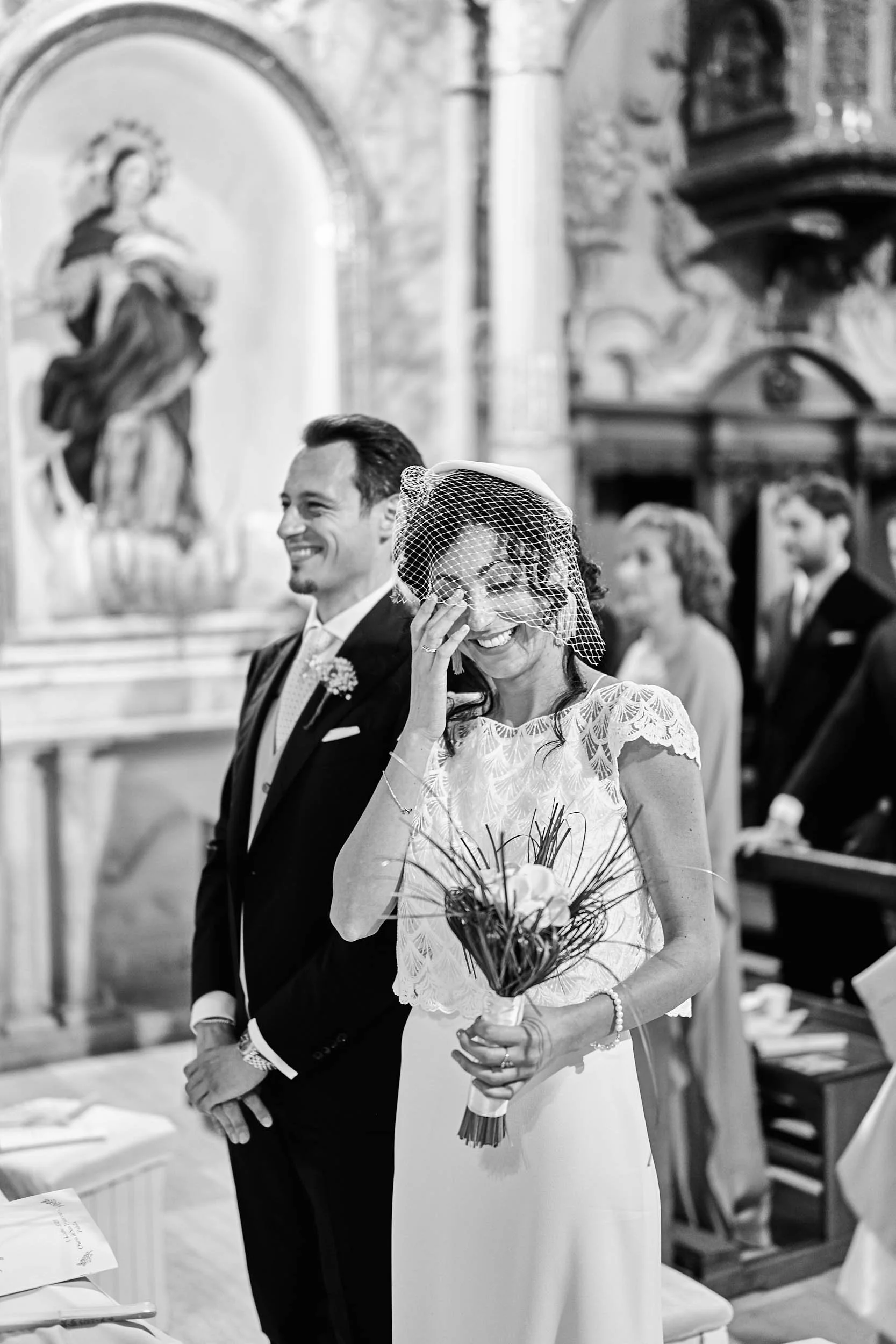 Bride smiling during the ceremony in a church, black and white wedding photography.