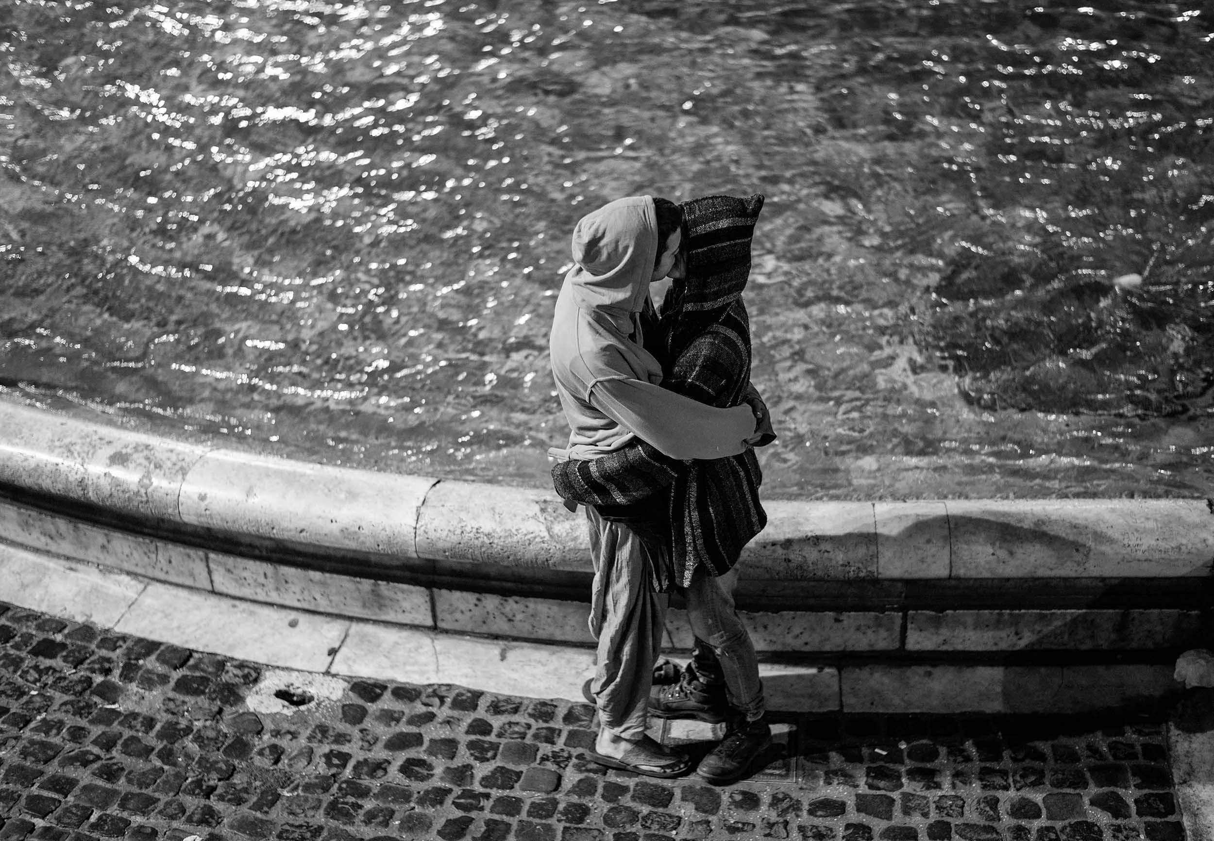 A couple kisses in front of a fountain. A black-and-white photo.