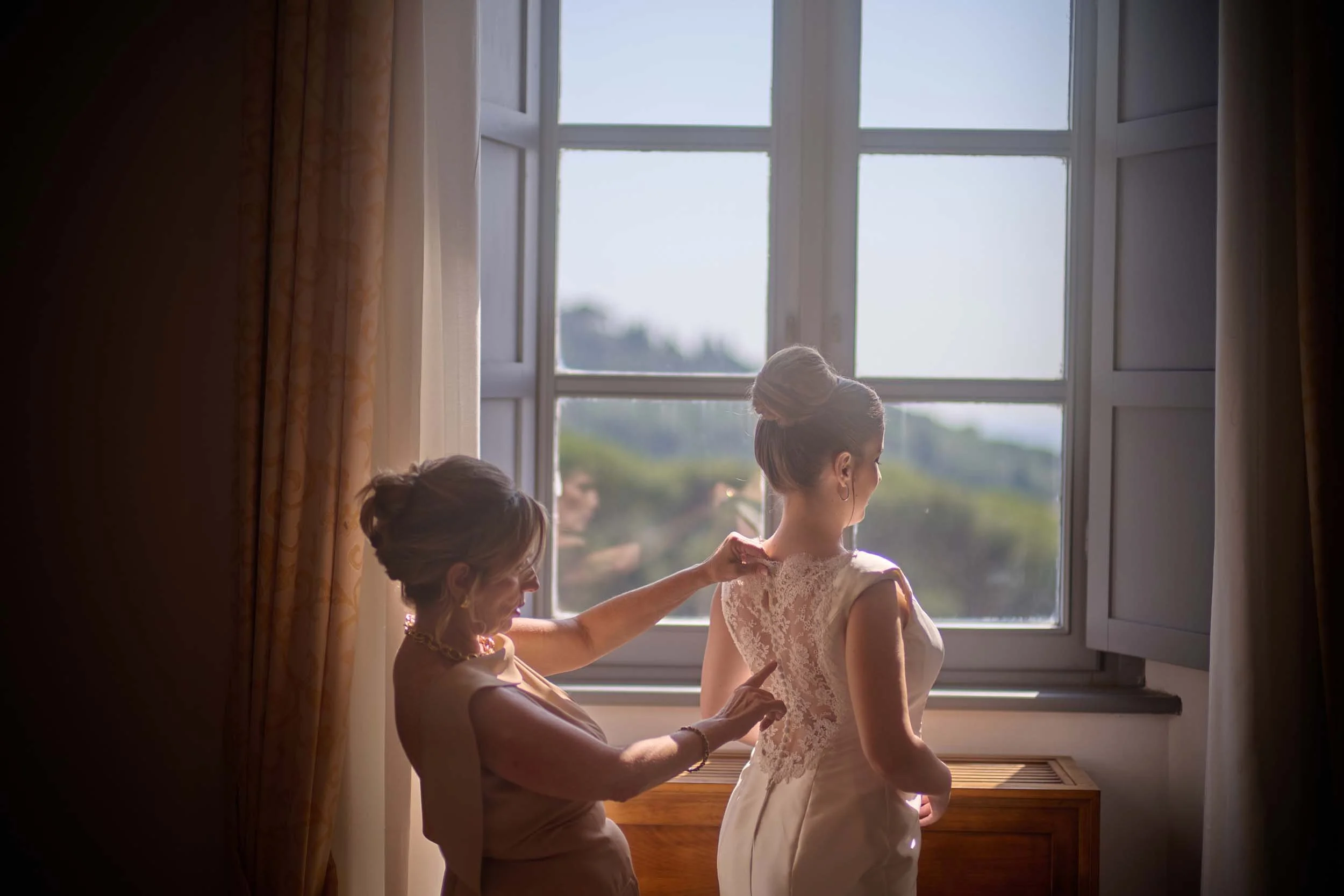 Mother fastening the bride’s dress, helping her get ready.