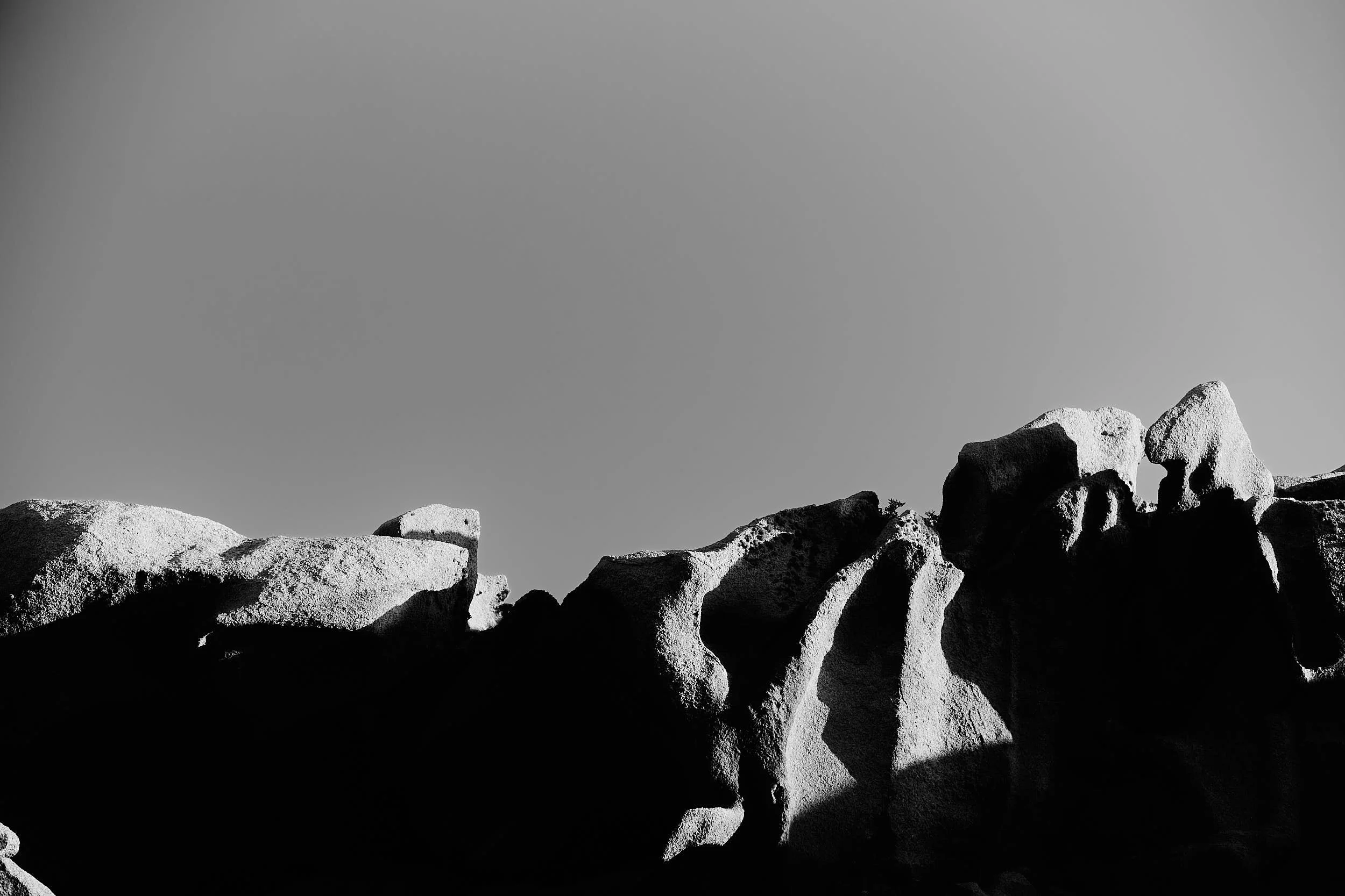 Graphic black-and-white landscape of sunlit granite boulders with deep shadows and a vast, clean sky — a quiet pause between moments.