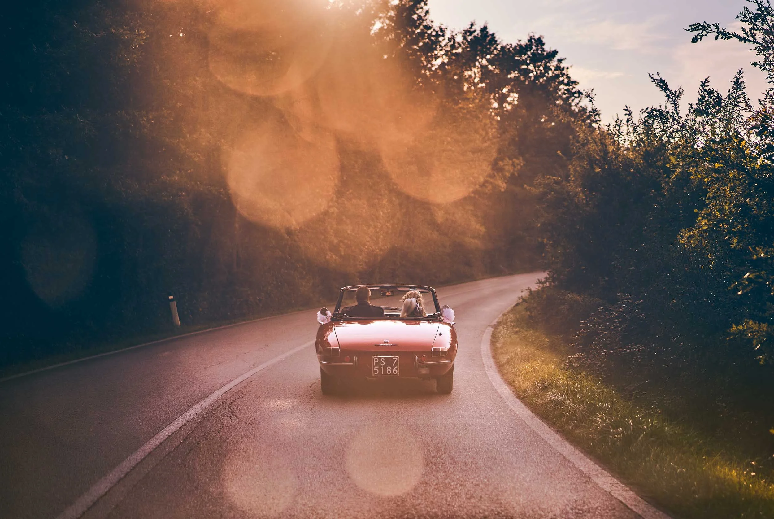 Newlyweds driving away in a vintage red convertible at sunset. The ultimate Italian destination wedding exit capturing freedom and romance.