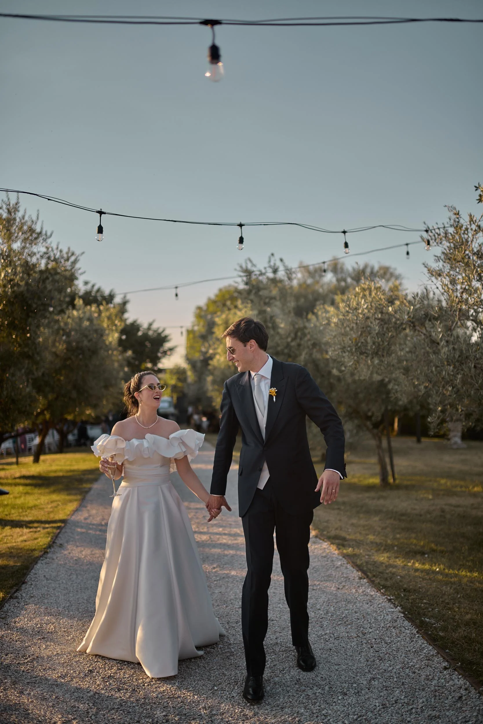 Happy bride and groom walking hand in hand through an olive grove at sunset, candid and unposed destination wedding photography in Umbria, near Todi.