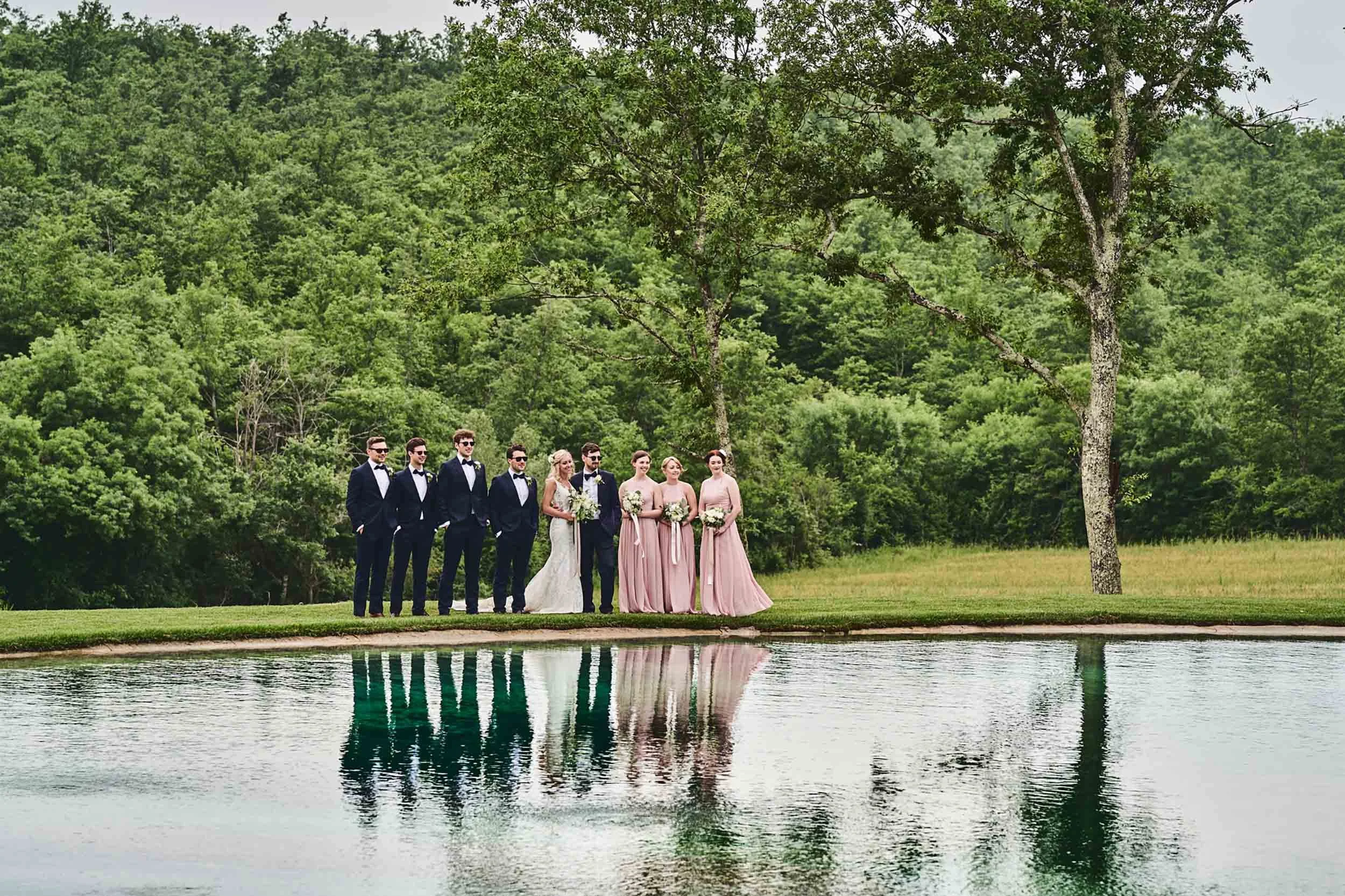 Bridesmaids, groomsmen, and the couple in a group portrait by the lake — intimate destination wedding in Tuscany