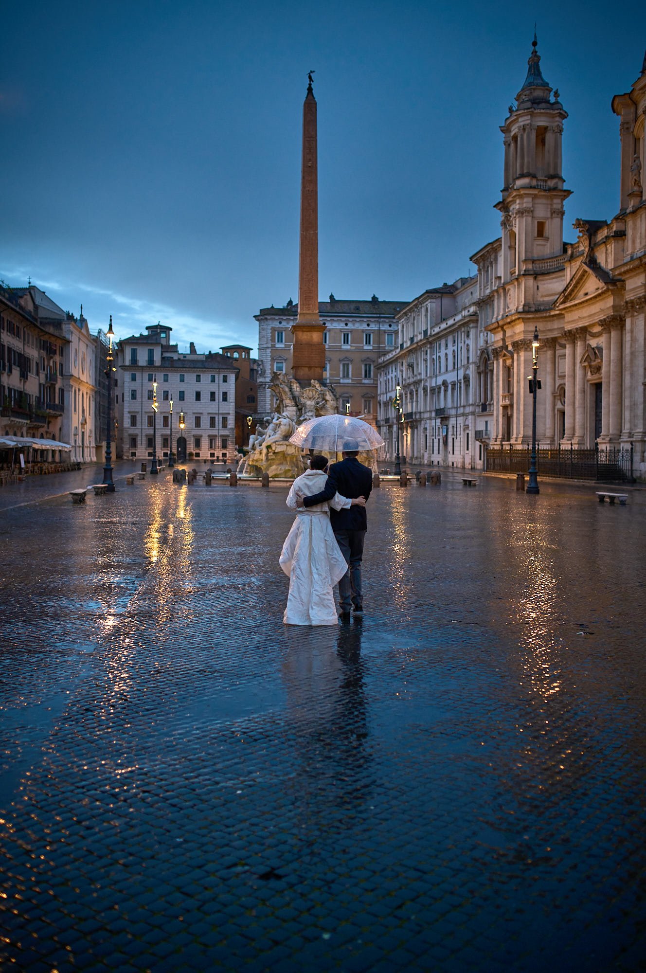 Bride and groom walking in Piazza Navona at dawn. Blue Hour, raining
