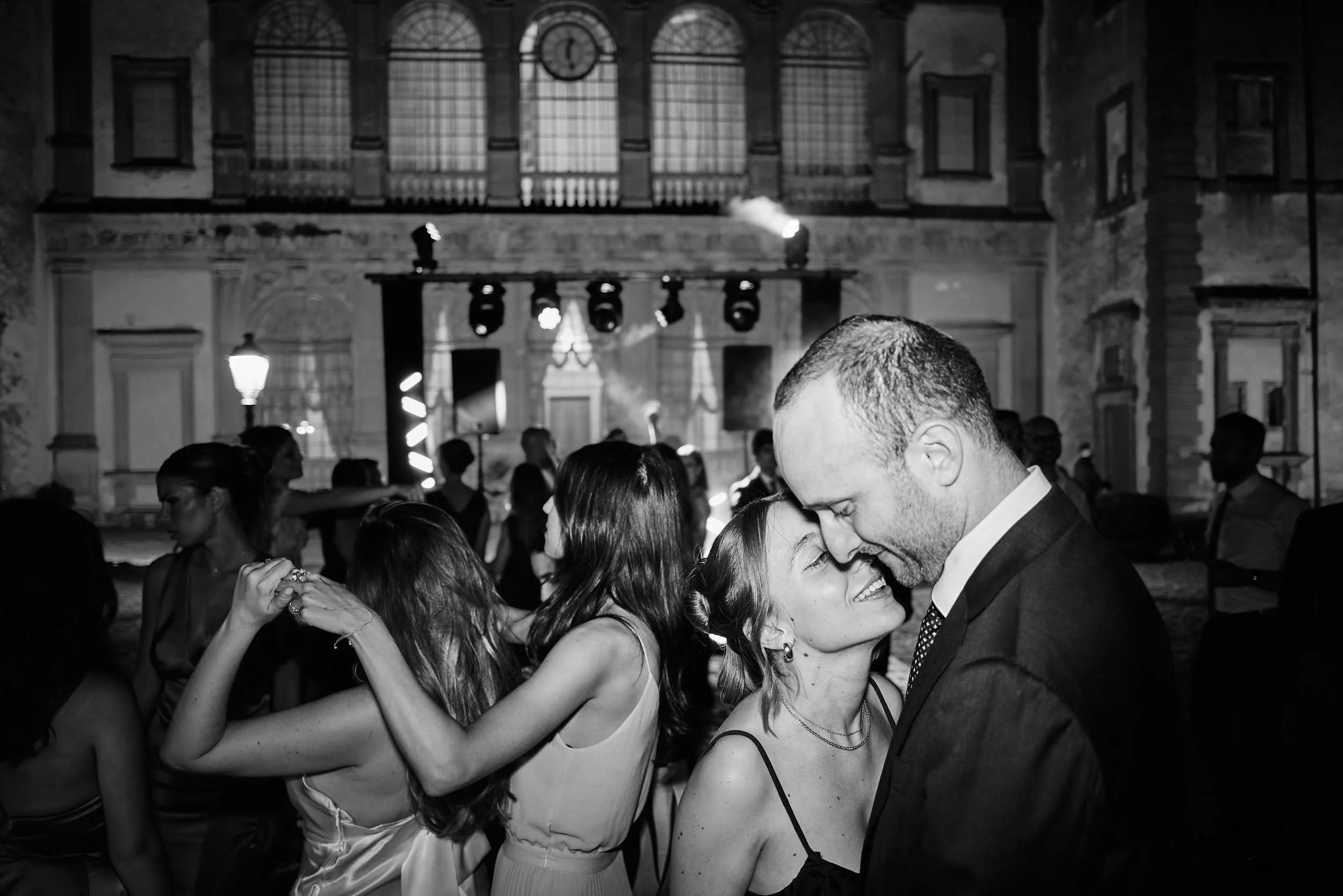 Young couple at the center of the dance floor in Villa Mondragone’s courtyard; she whispers to him sweetly.