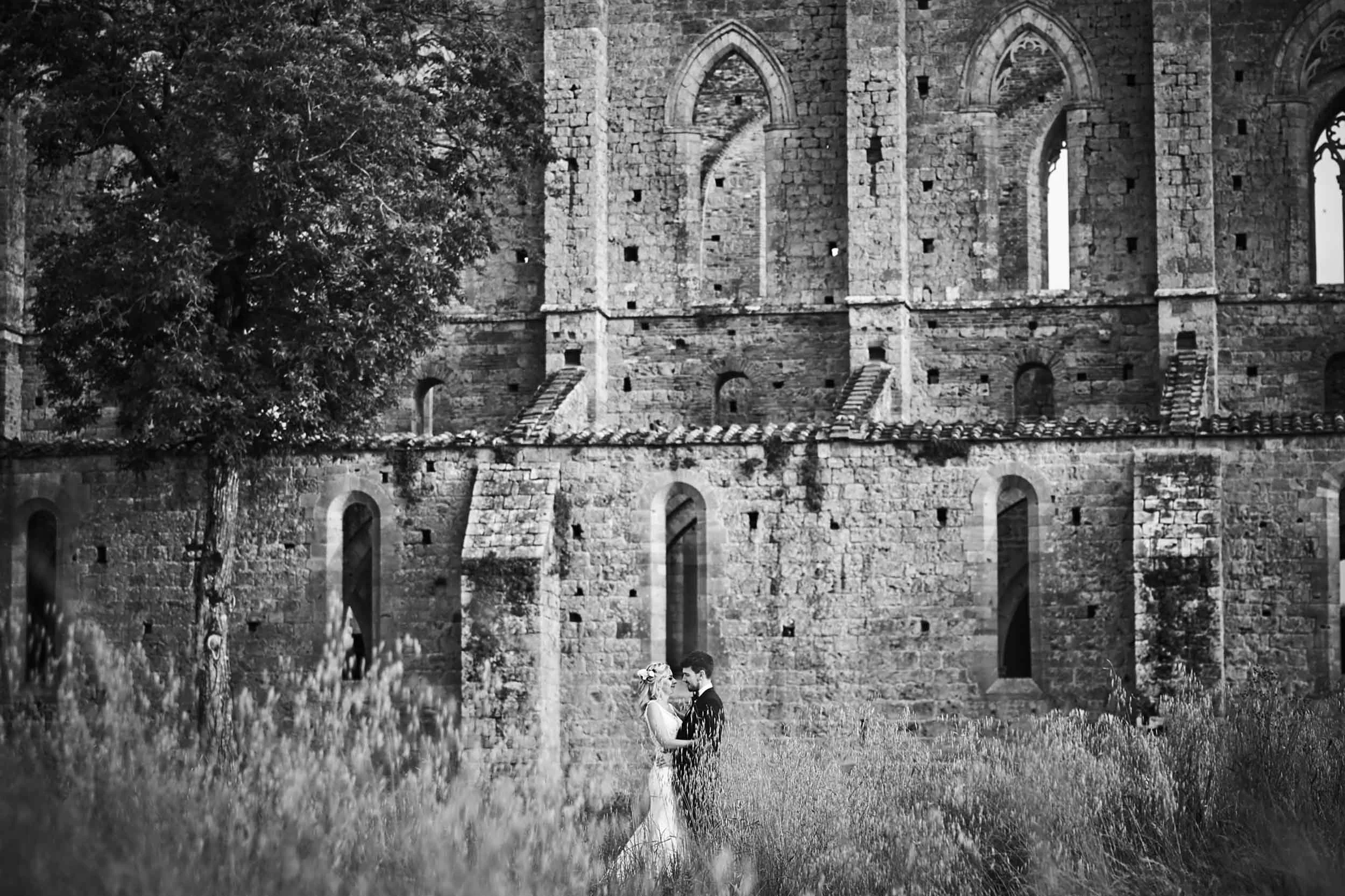 Black and white portrait of the couple in nature with San Galgano Abbey in the background — Tuscany