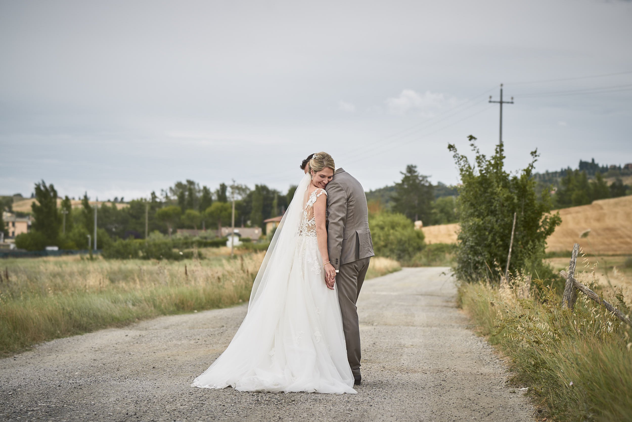 Destination wedding portrait in Tuscany: the couple holding hands on a quiet country road, hills and fields behind them
