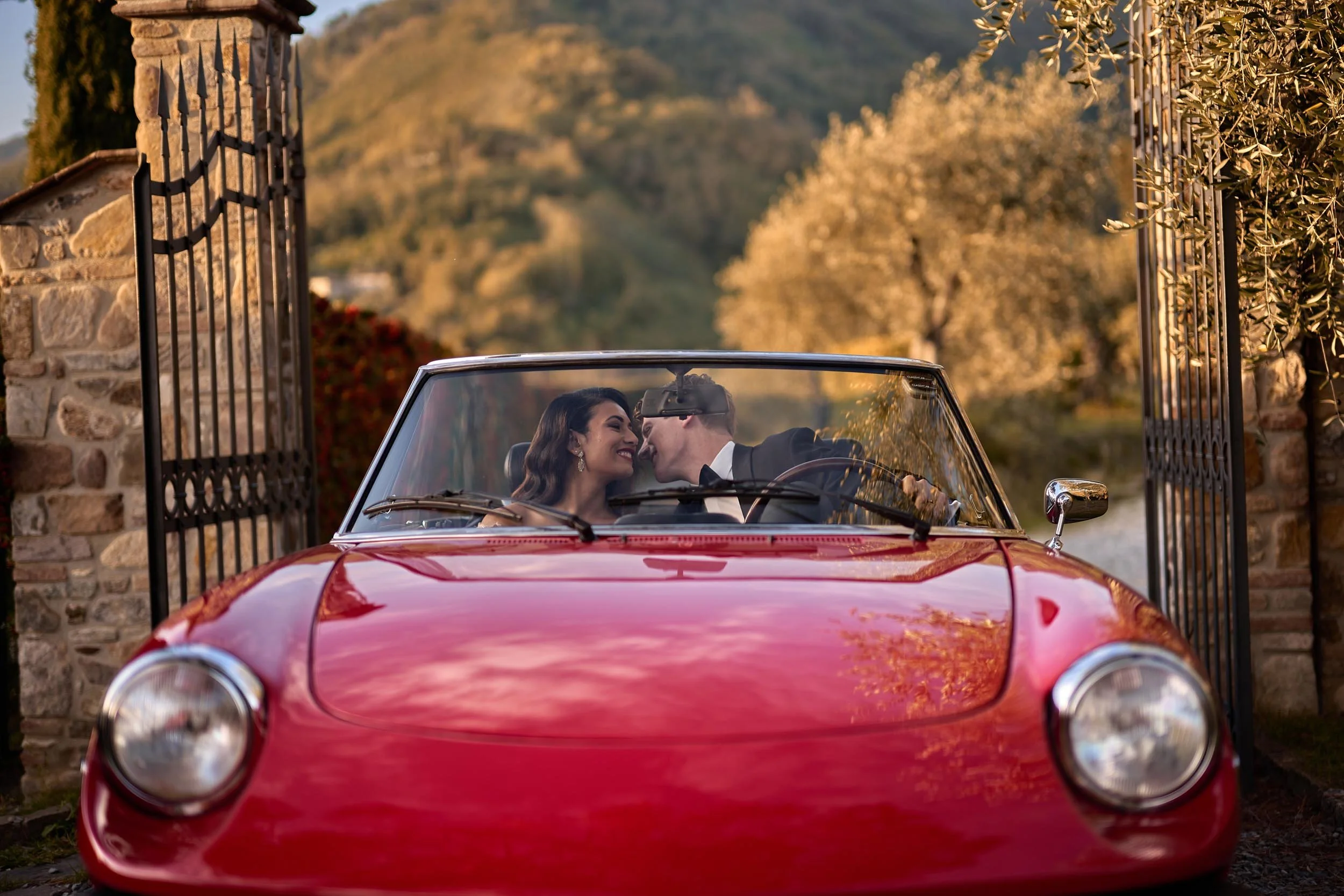 Groom whispers to the bride in the red Alfa Spider while arriving — intimate destination wedding