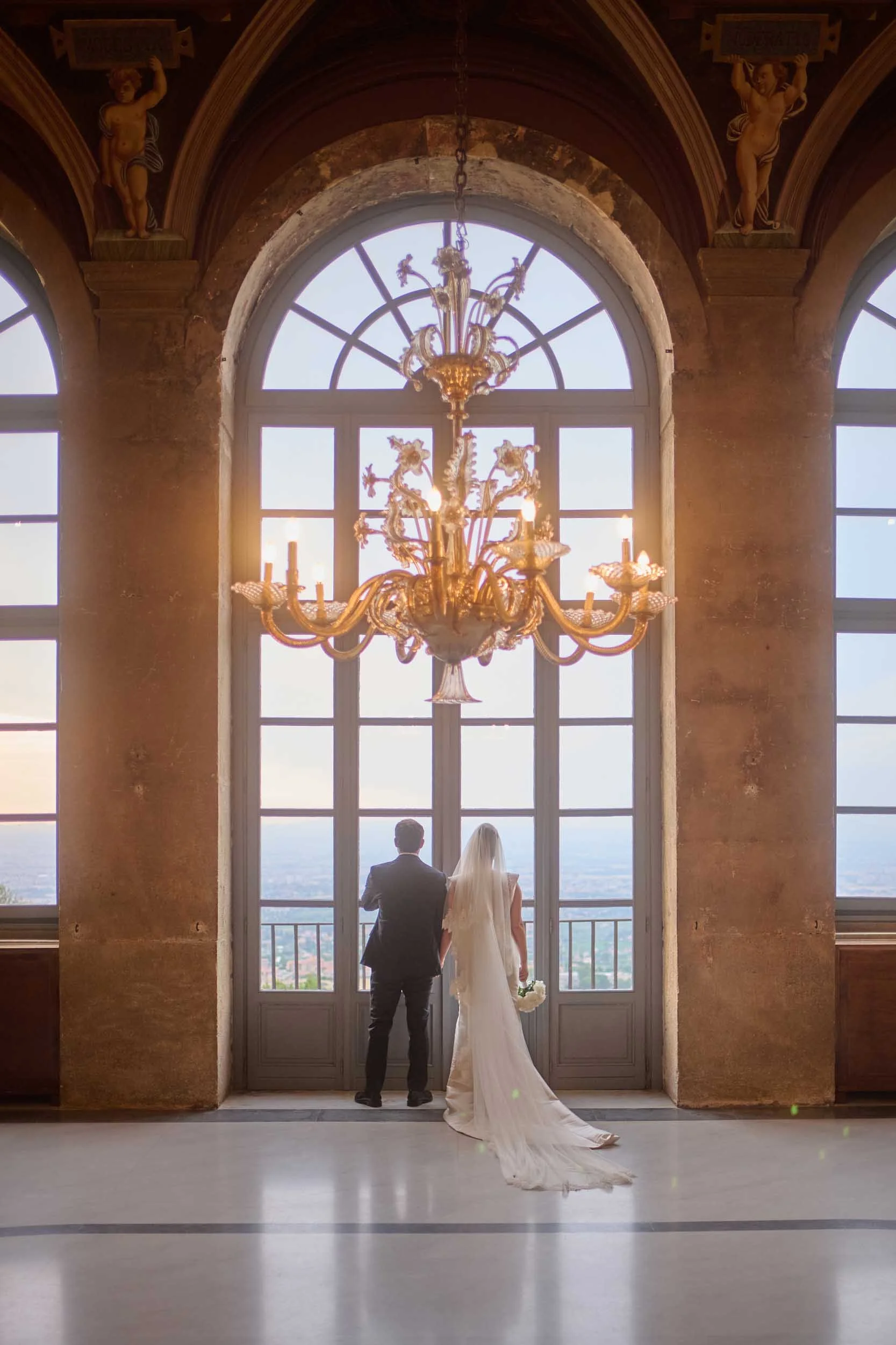 Backlit: young newlyweds gaze at the horizon from a window in Villa Mondragone’s hall adorned with 14th-century frescoes.
