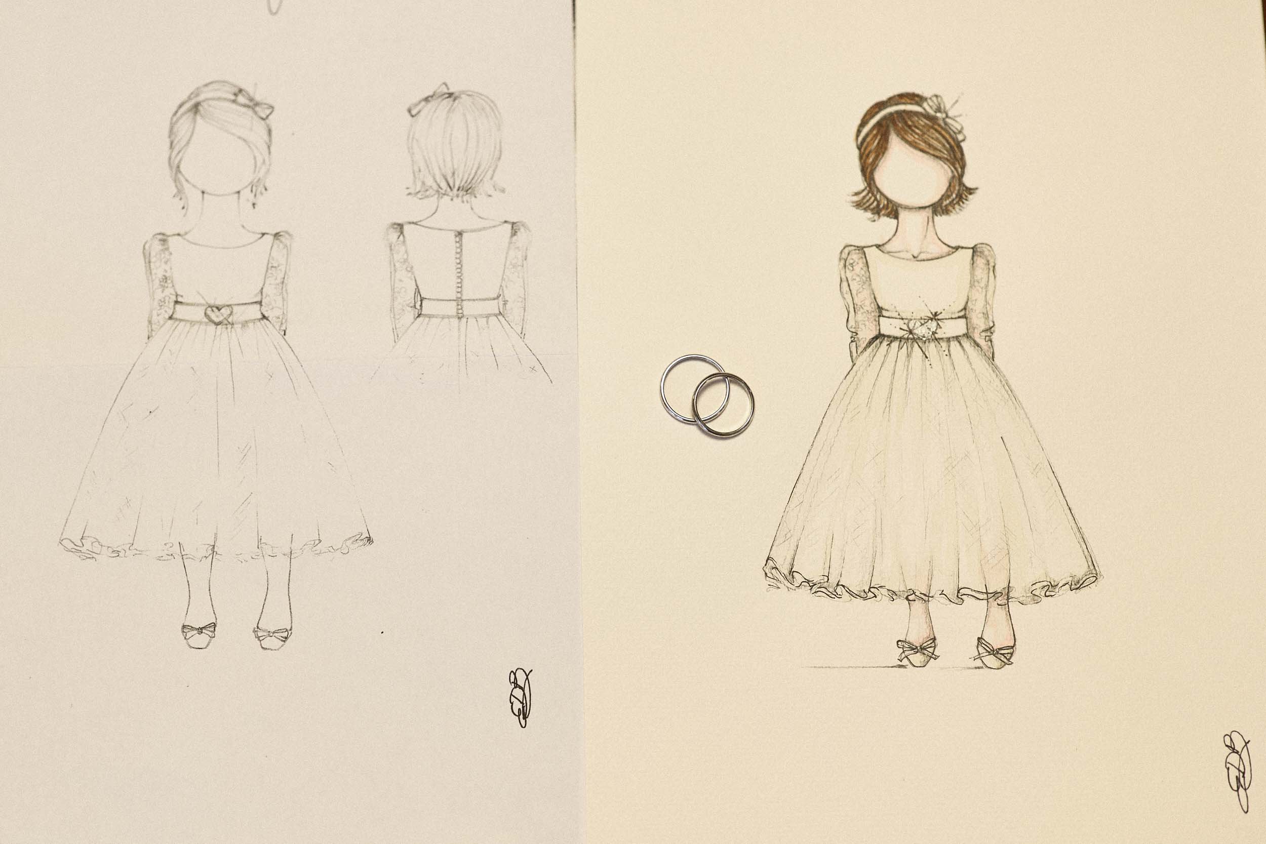 Two wedding rings resting on an illustrated dress design sketch, photographed as a minimal detail still life.