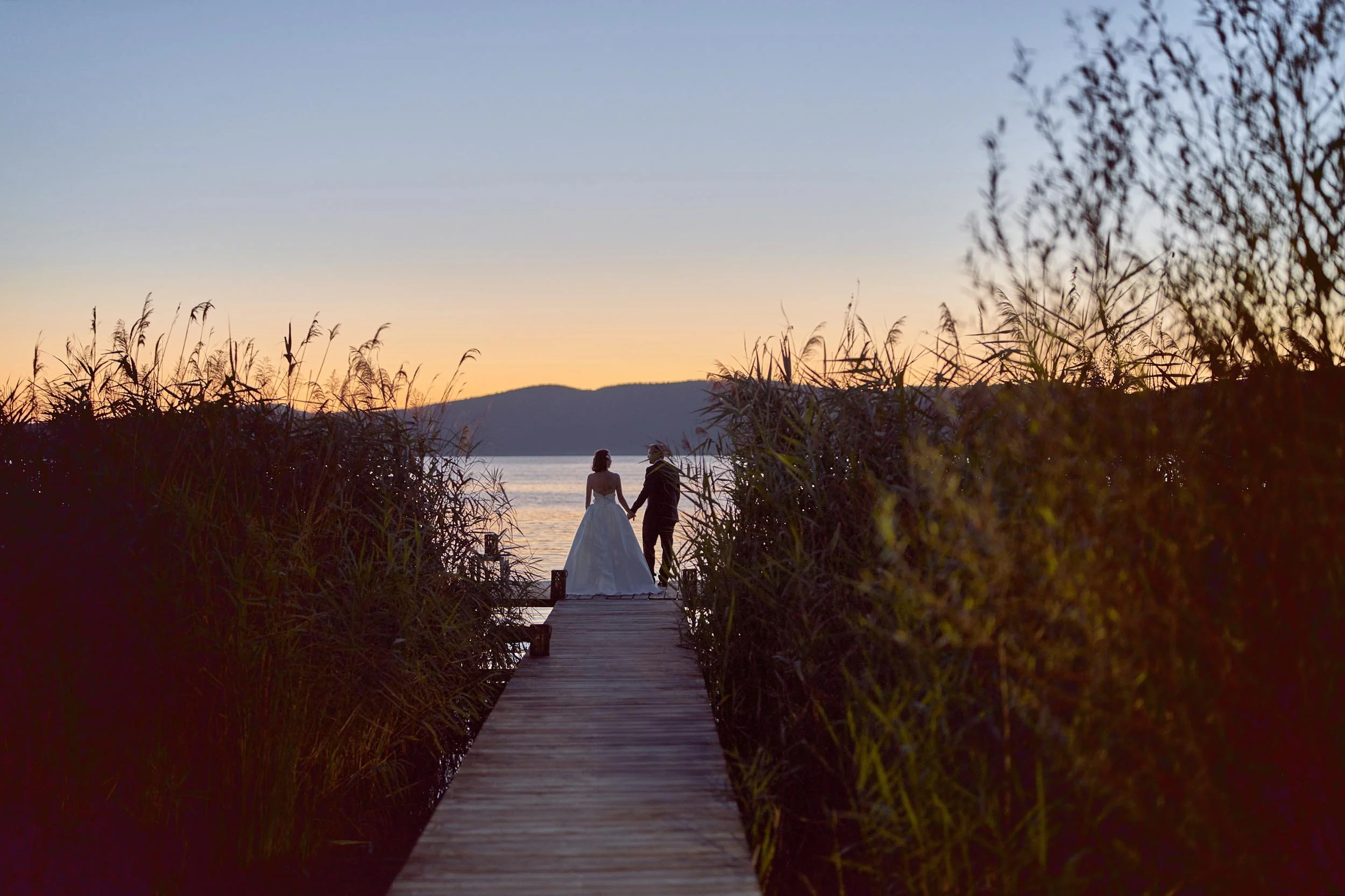 A quiet moment at sunset: bride and groom on a wooden pier at Tenuta di Polline, Italy.