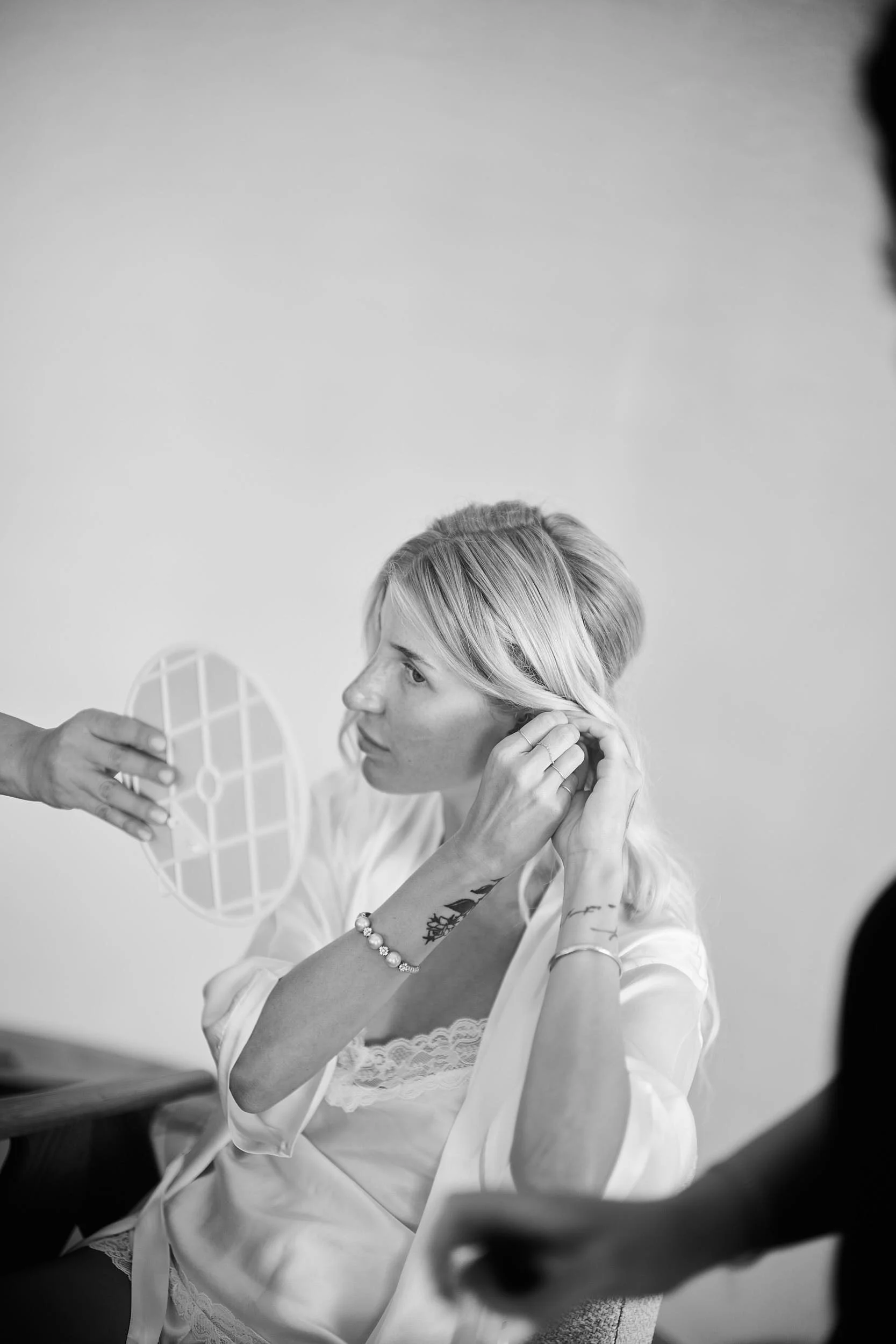 Bride adjusting her earring while a mirror is held nearby during getting ready.