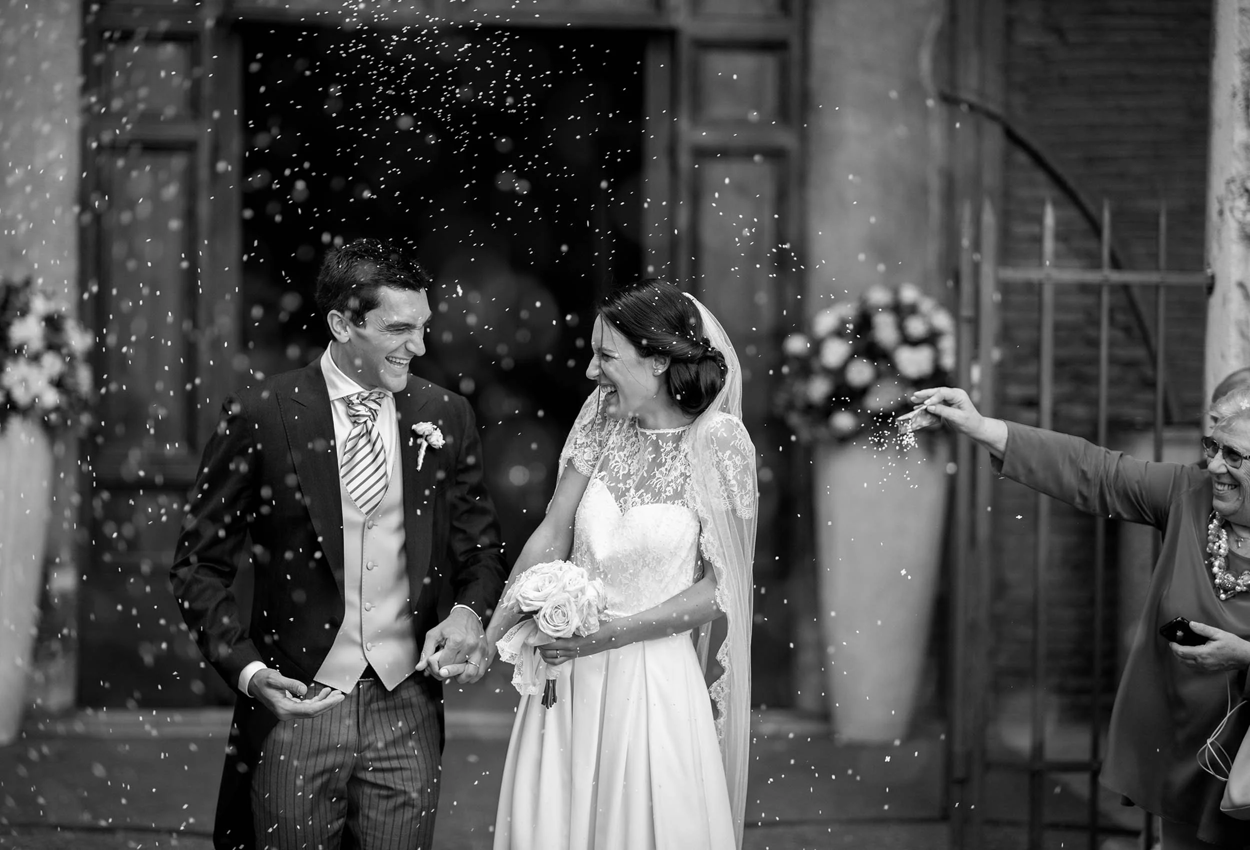 Joyful black and white photo of bride and groom leaving the church under a shower of rice. Authentic wedding reportage in Rome capturing real emotions.