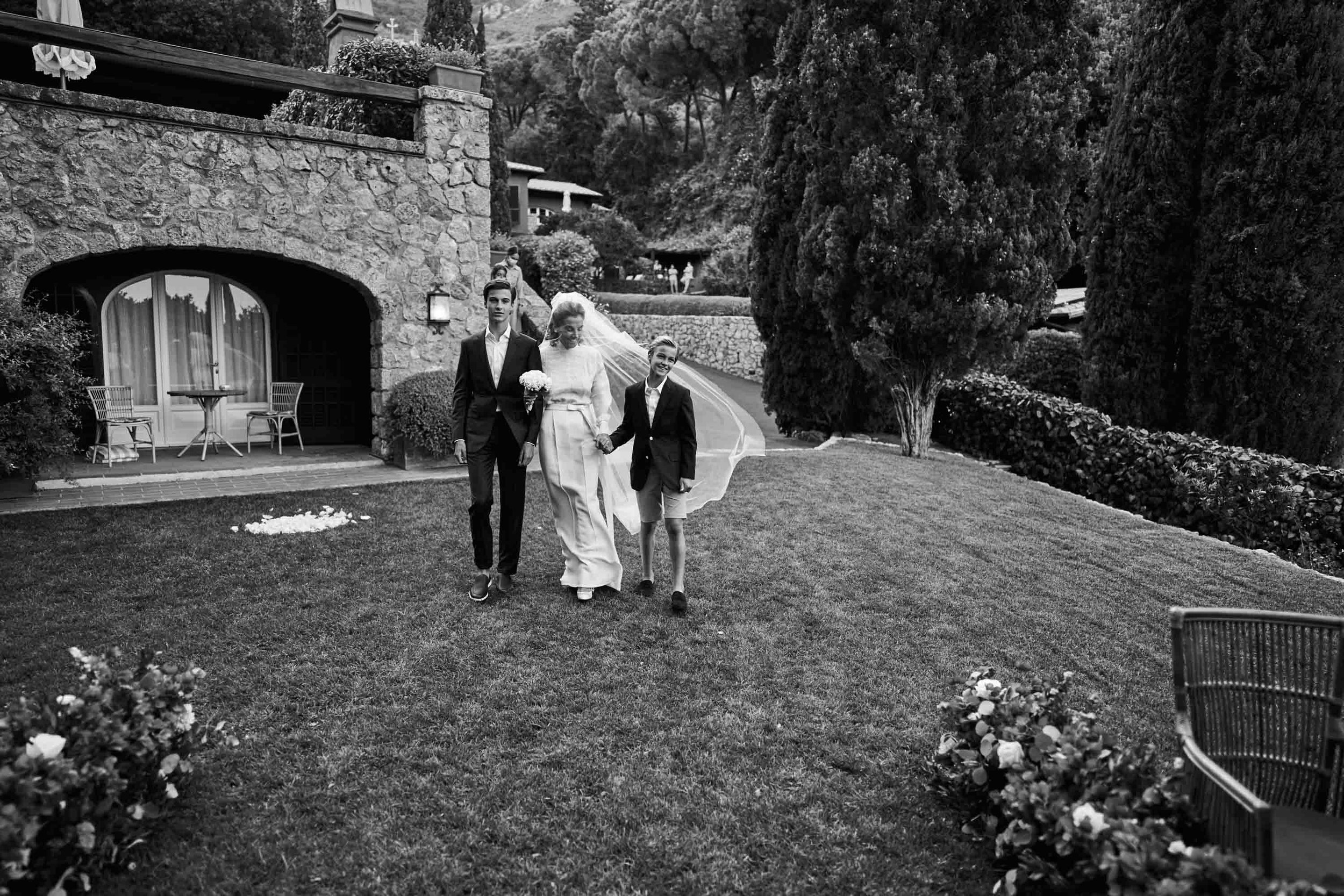 Intimate destination wedding in Italy — bride walking to the ceremony with her sons at Hotel Il Pellicano (black and white).