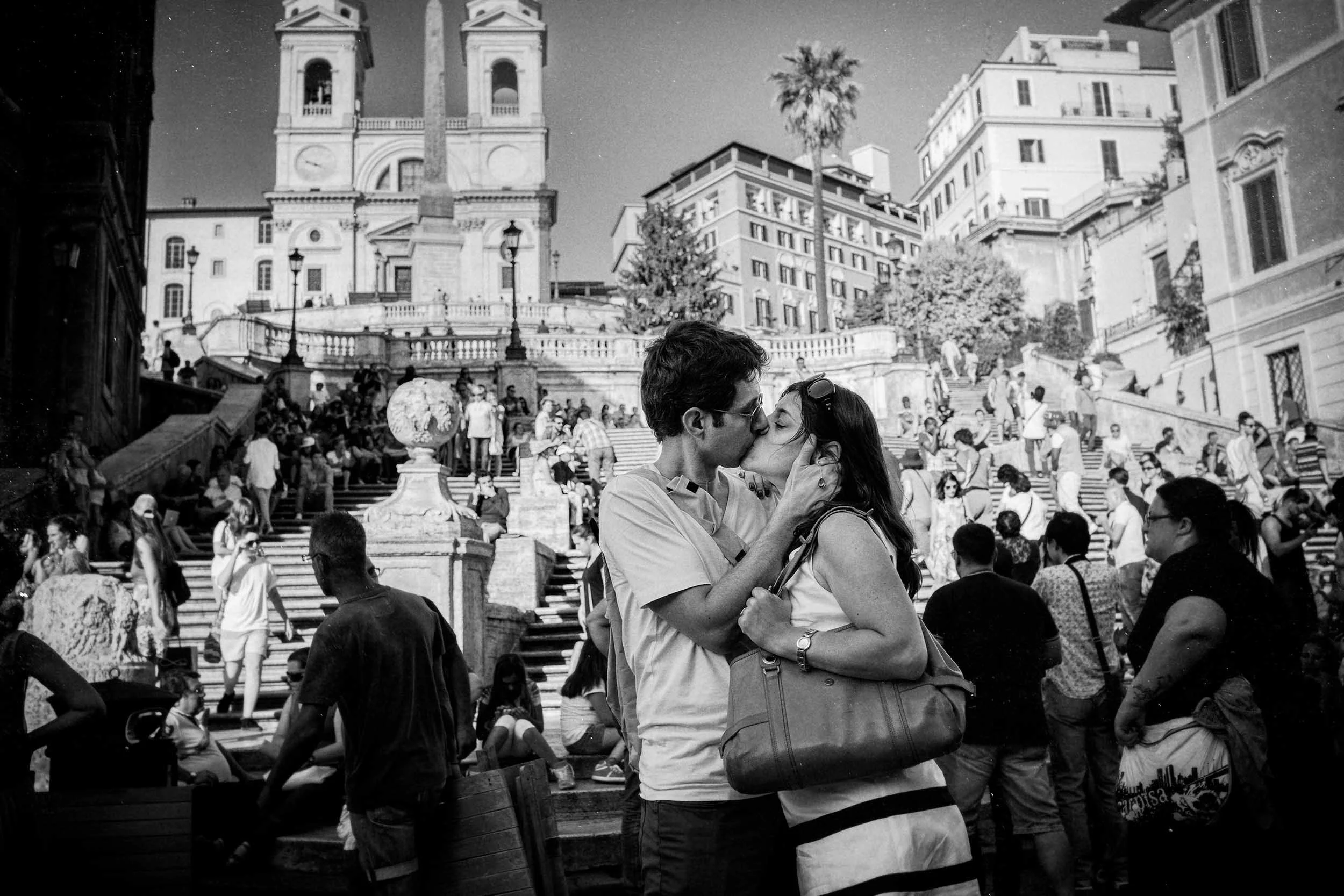 A couple kissing in Piazza di Spagna, Rome, in a black-and-white photograph.