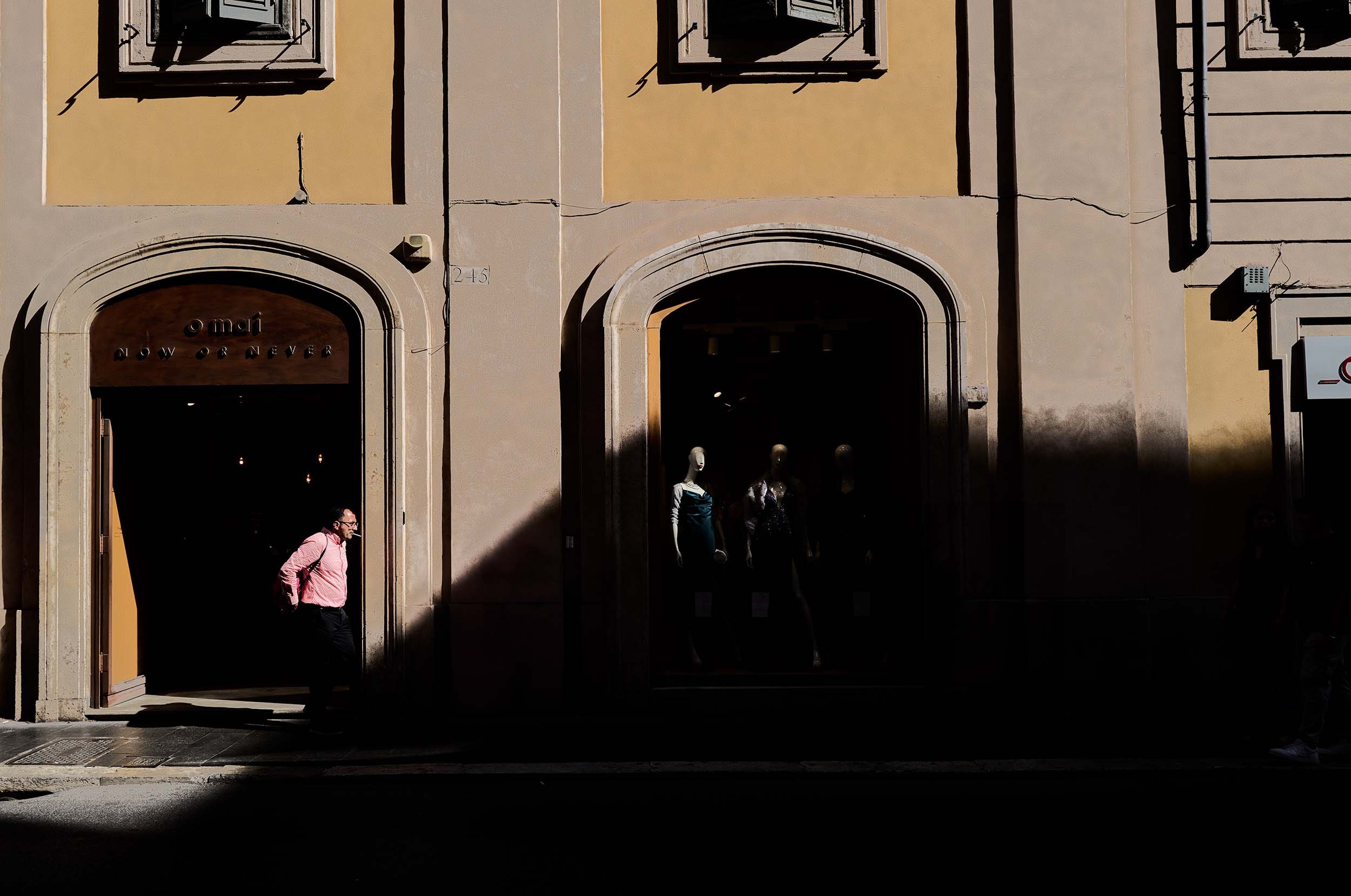 A man smoking a cigarette while walking between shadows and lights.