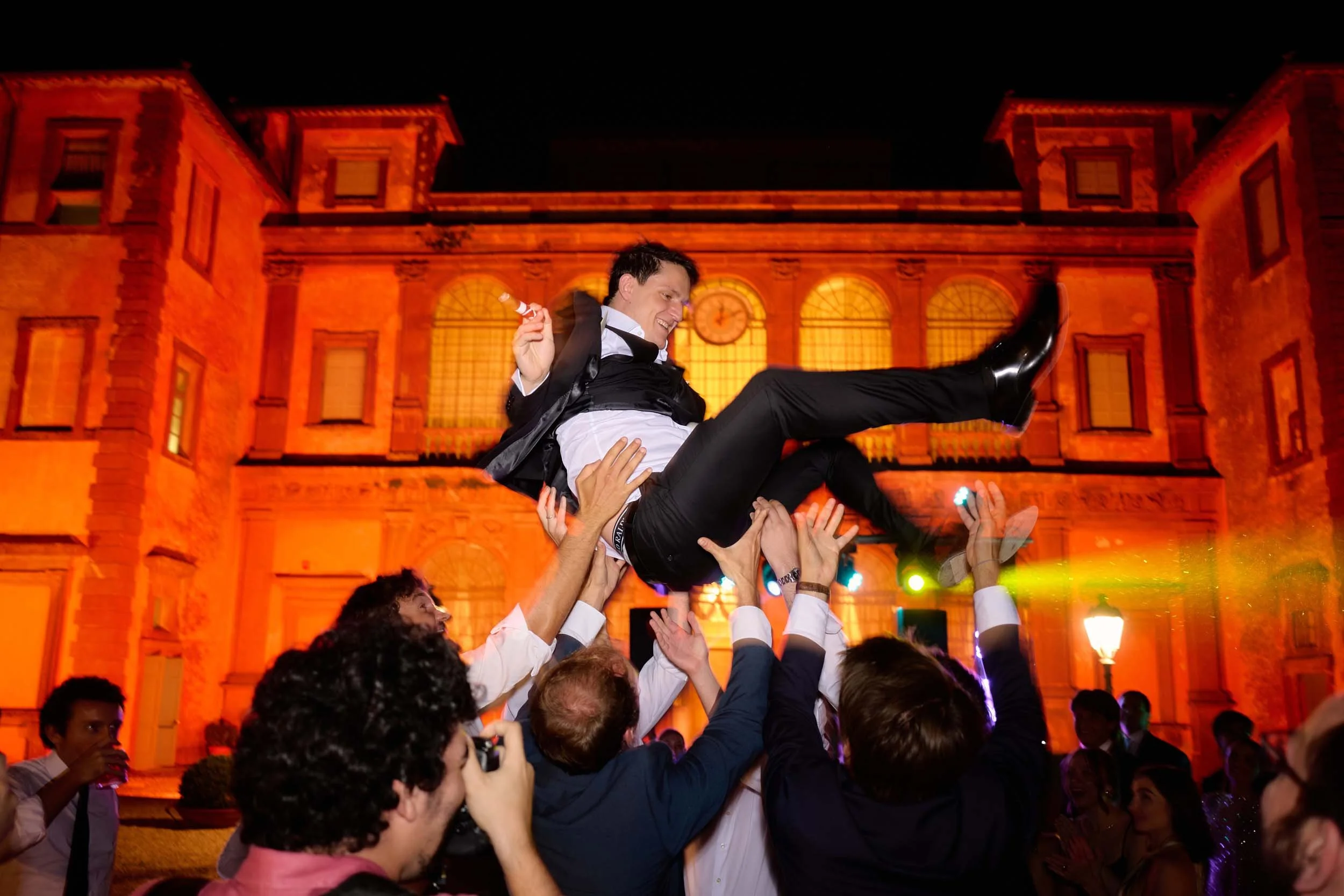 Groom thrown into the air by his friends, courtyard facade of Villa Mondragone in view.