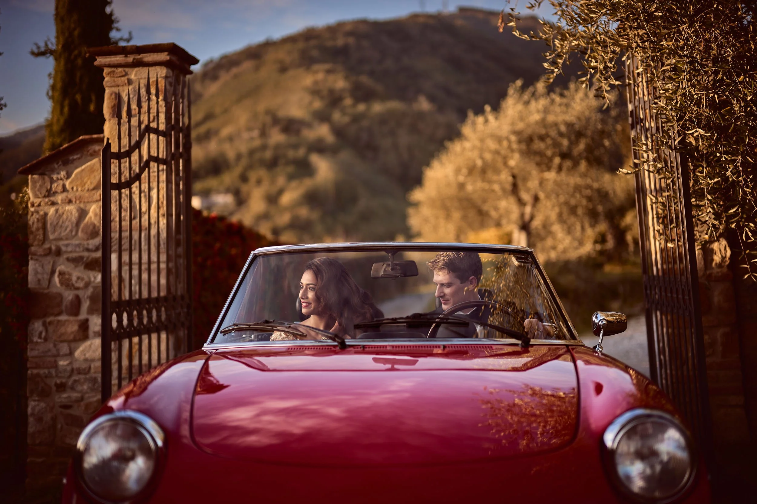 Bride and groom driving a red Alfa Romeo at sunset near Lucca — intimate Indian destination wedding in Tuscany