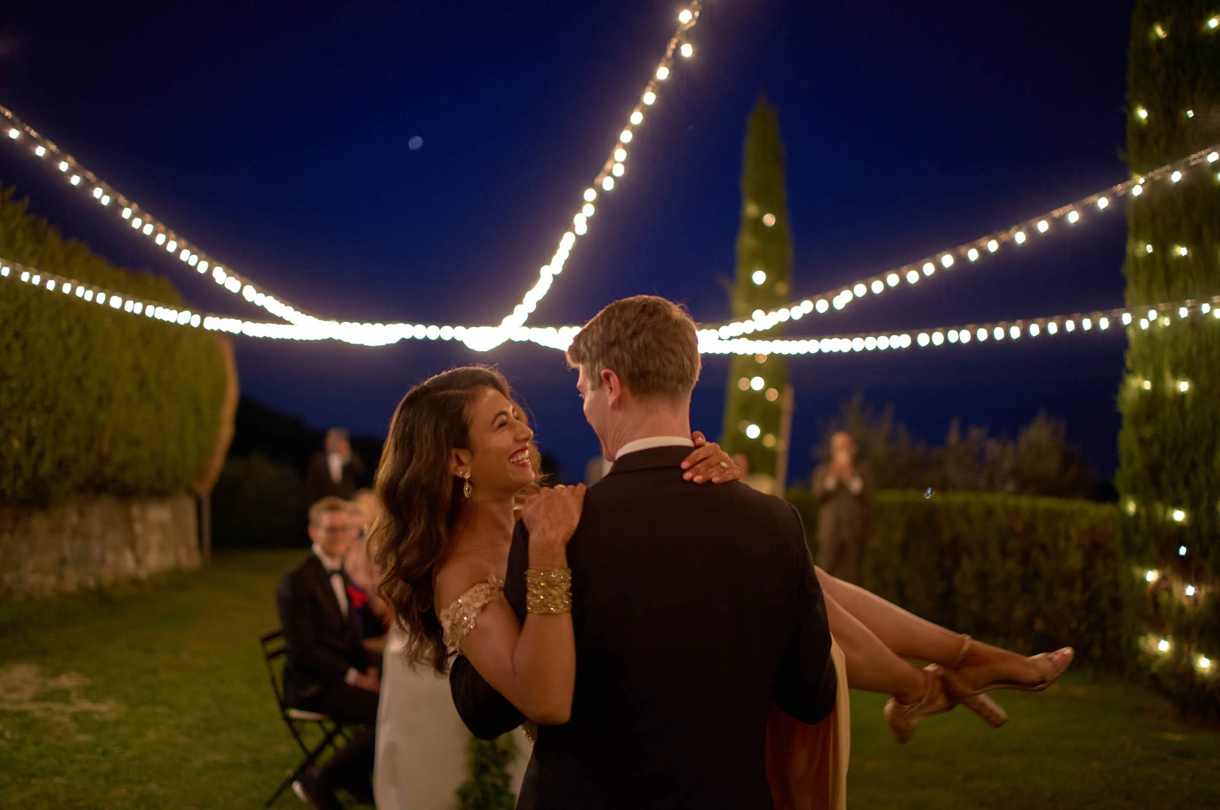 Groom lifts the bride during the first dance — blue hour and warm lights, intimate wedding near Lucca