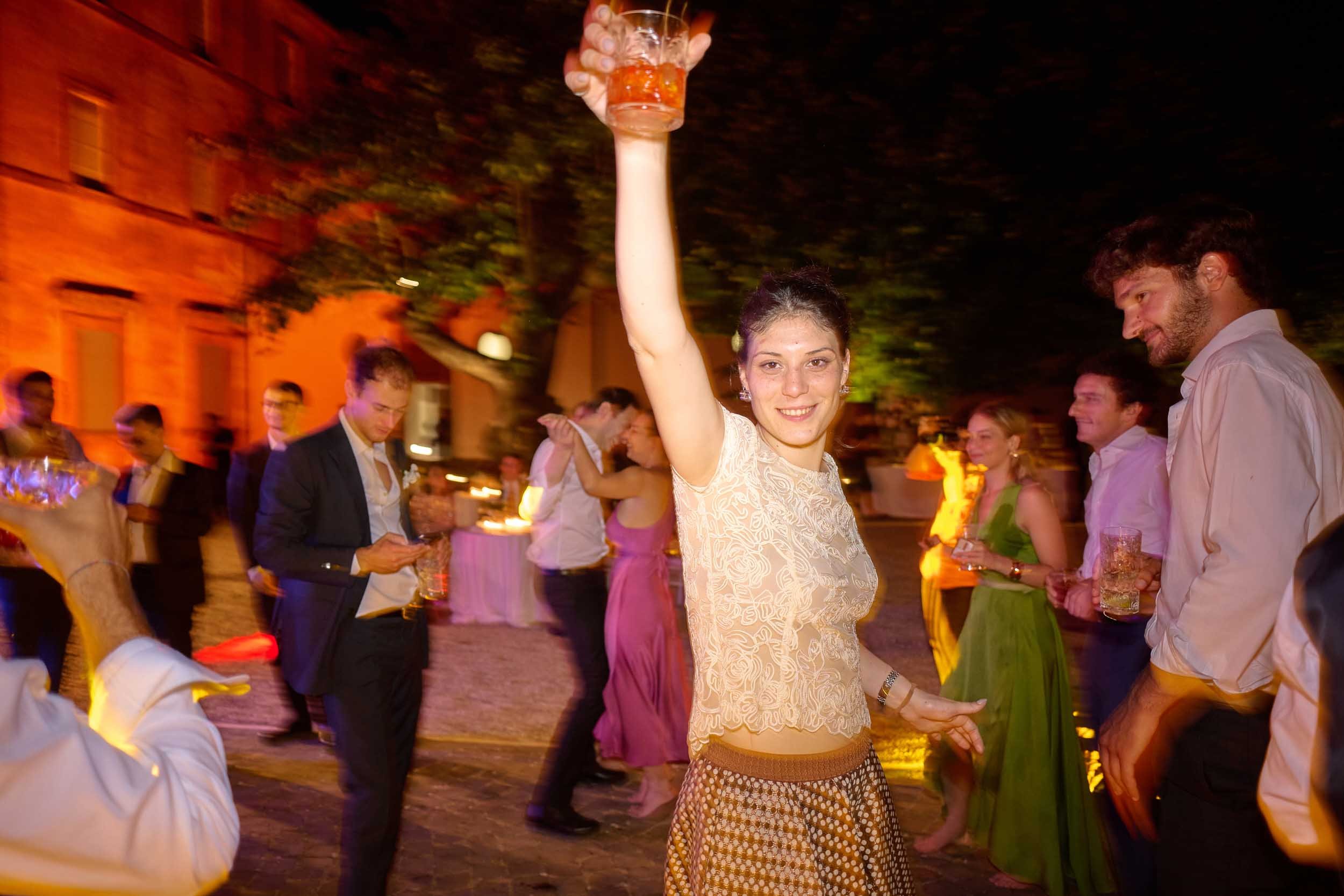 Friendly, smiling young woman raises her glass toward the photographer on the dance floor.