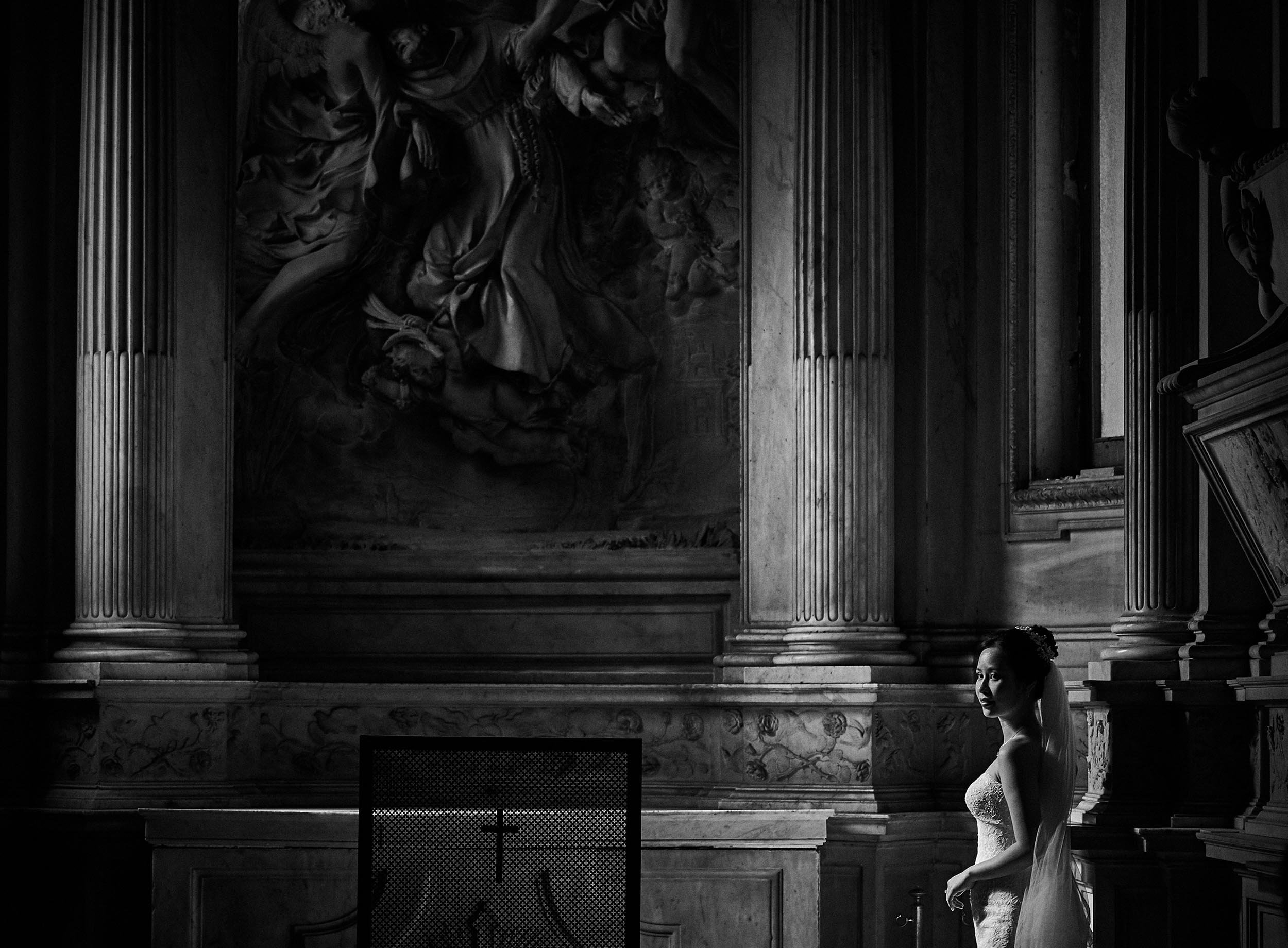 Cinematic wedding portrait of a bride standing inside a monumental Roman church. High contrast black and white composition emphasizing the scale of Rome's architecture.