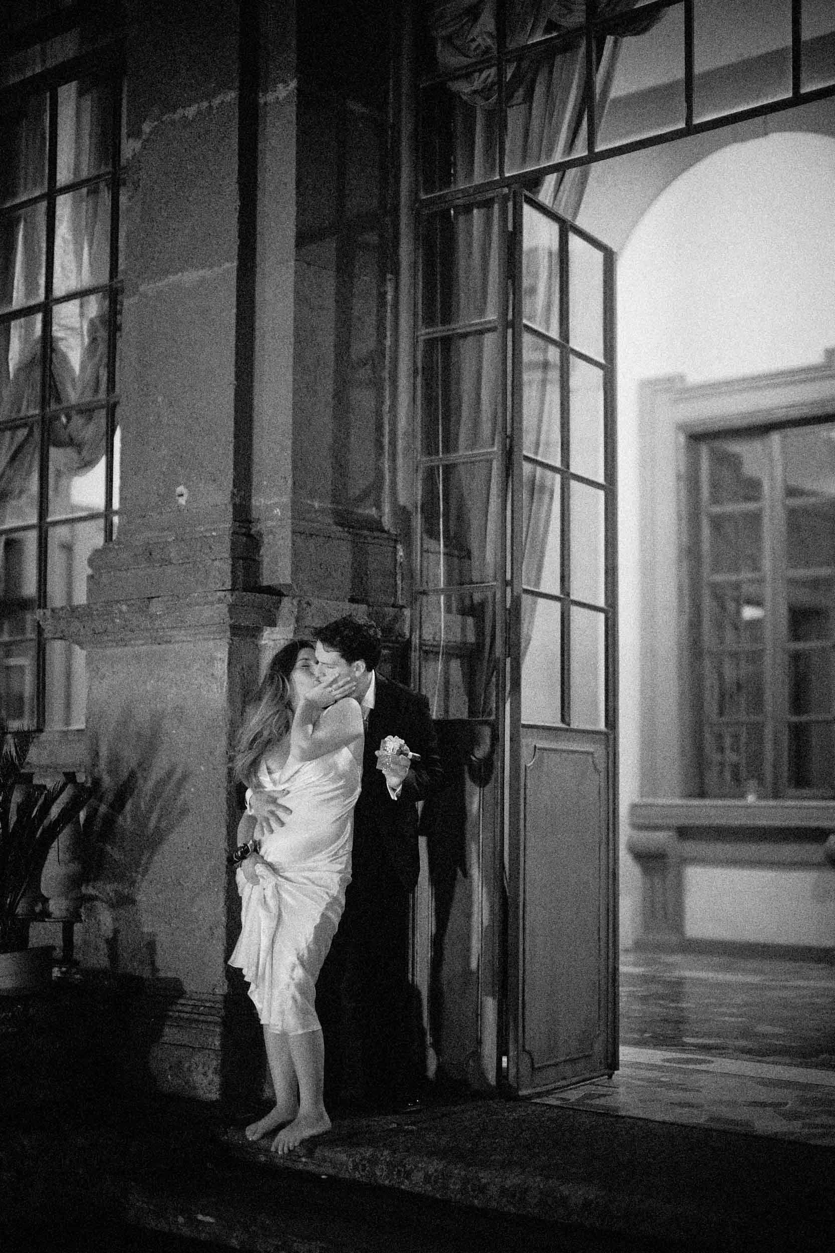 Passionate kiss at Villa Mondragone’s entrance at night; the groom cradles the bride’s belly—she’s expecting