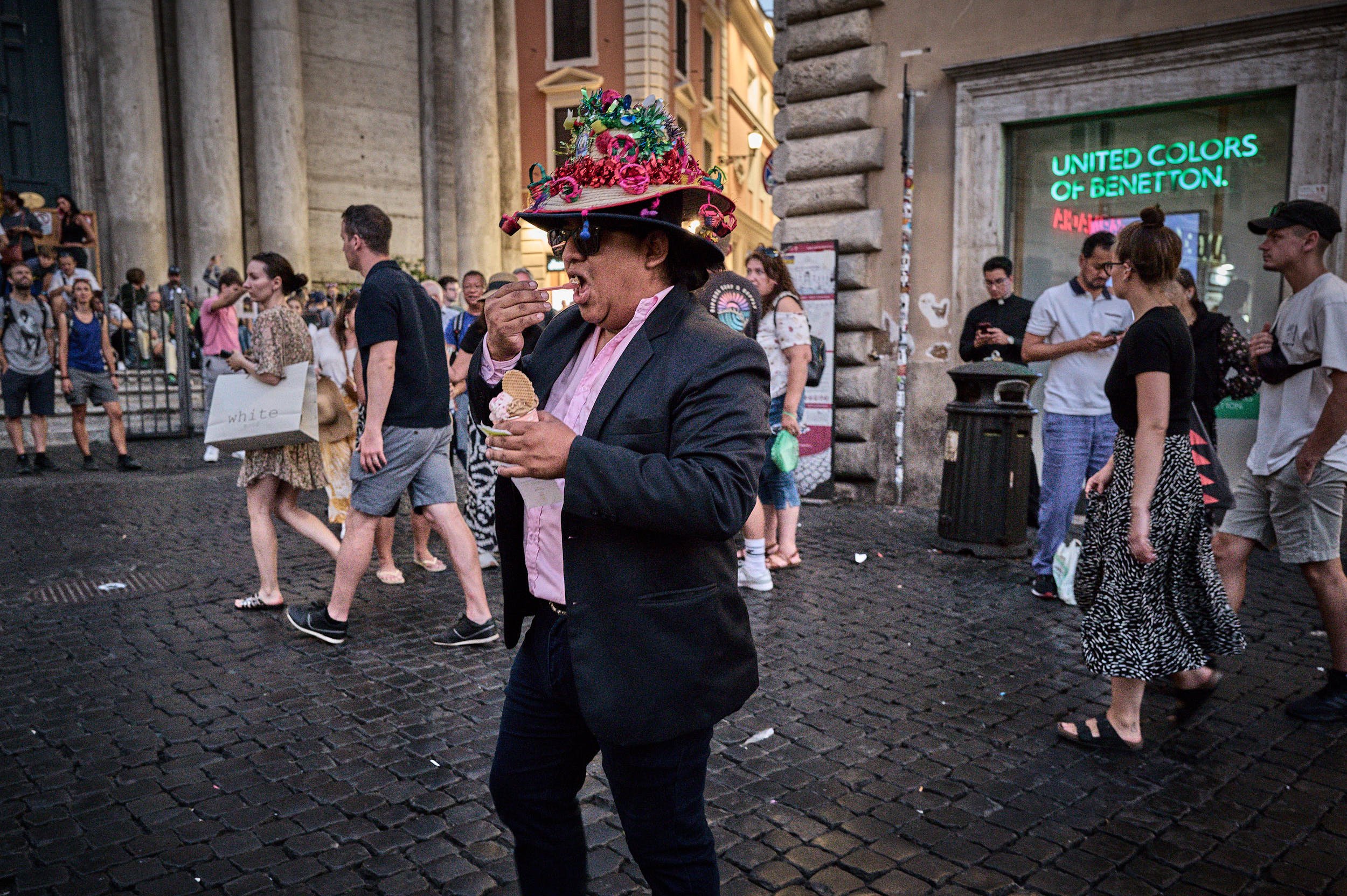 A man eating an ice cream, wearing a strange, colorful hat