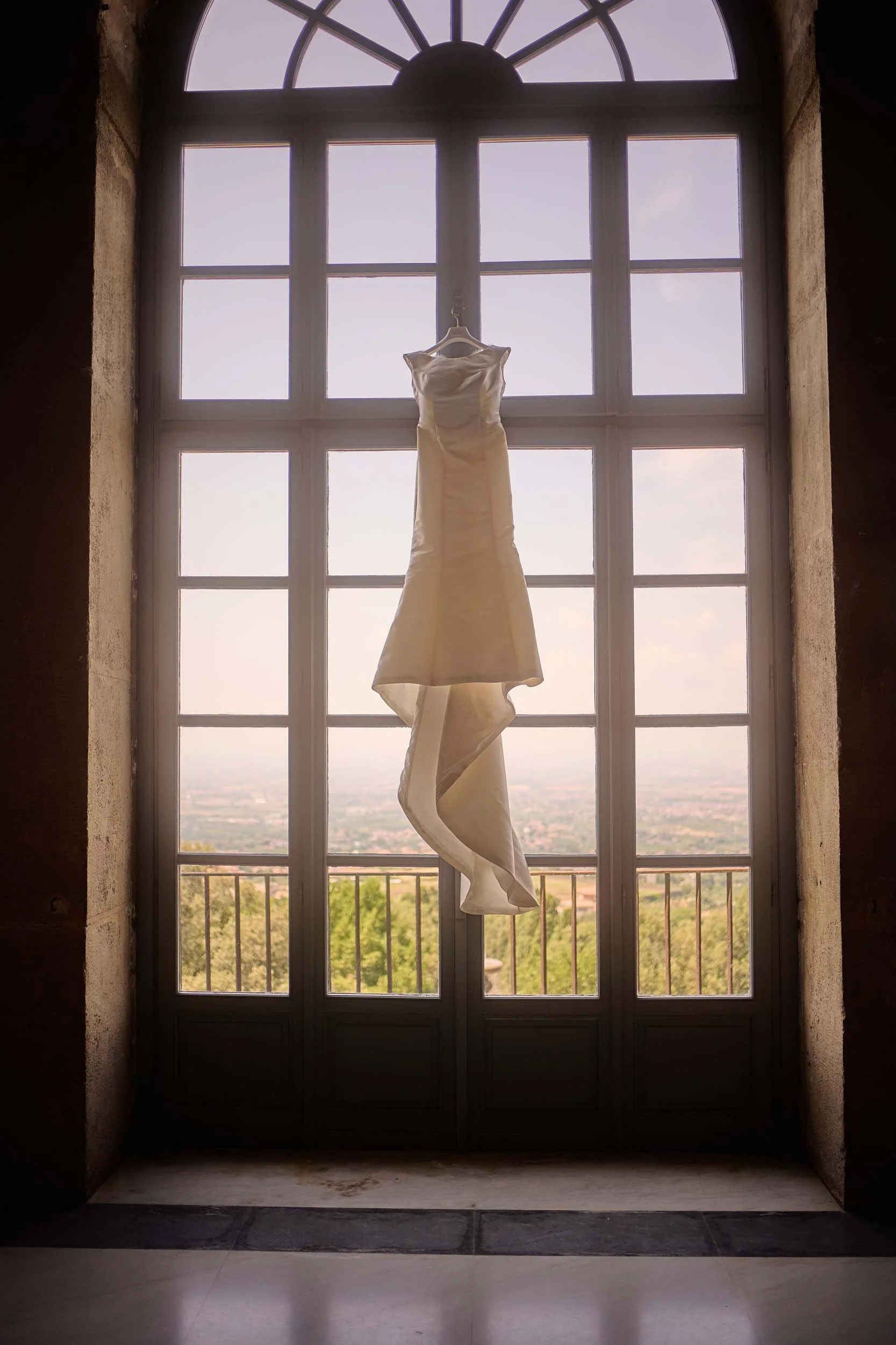 The bride’s dress hangs from a window at Villa Mondragone with a view toward Rome
