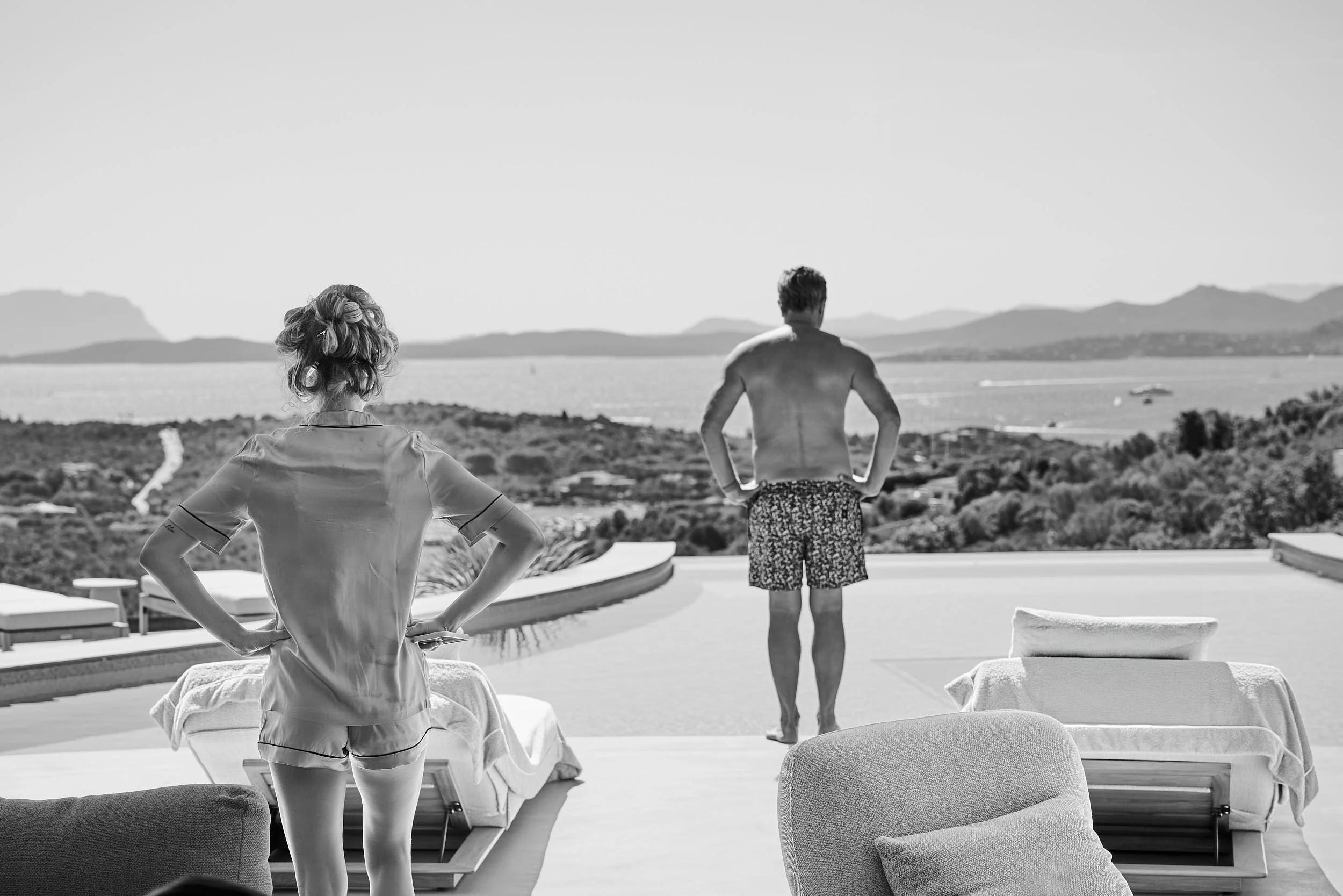 Two wedding guests by the pool, looking out over the sea and distant islands in Sardinia.