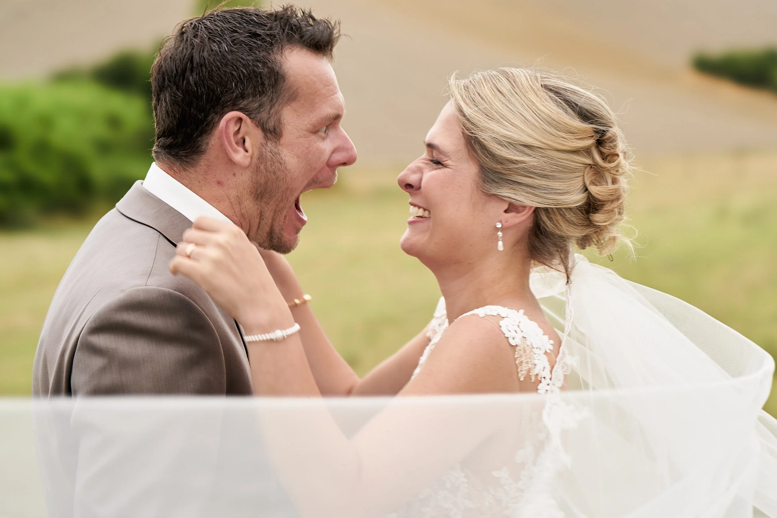 Close-up of the couple laughing and teasing each other during portraits, with soft Tuscan hills in the background.