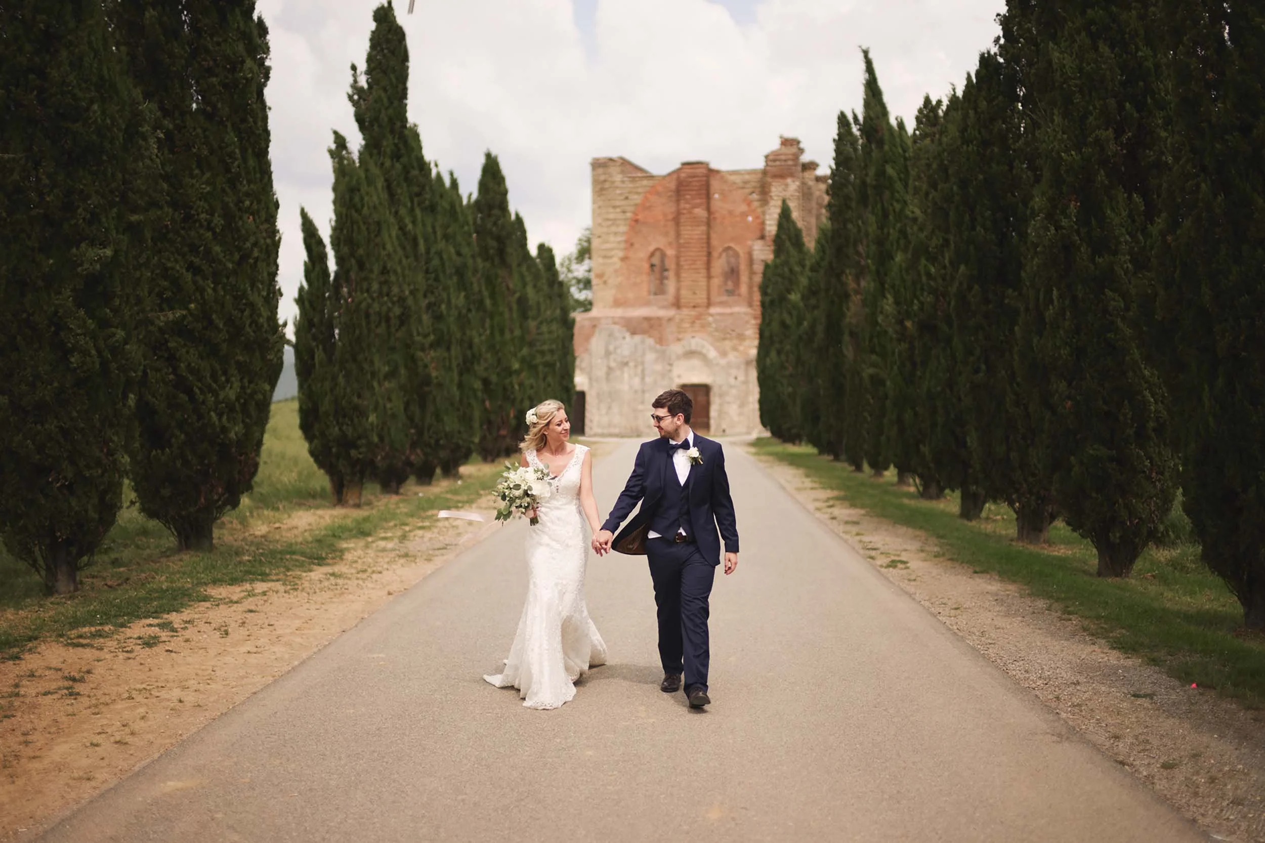 Bride and groom walking away hand in hand near San Galgano Abbey — intimate destination wedding in Tuscany