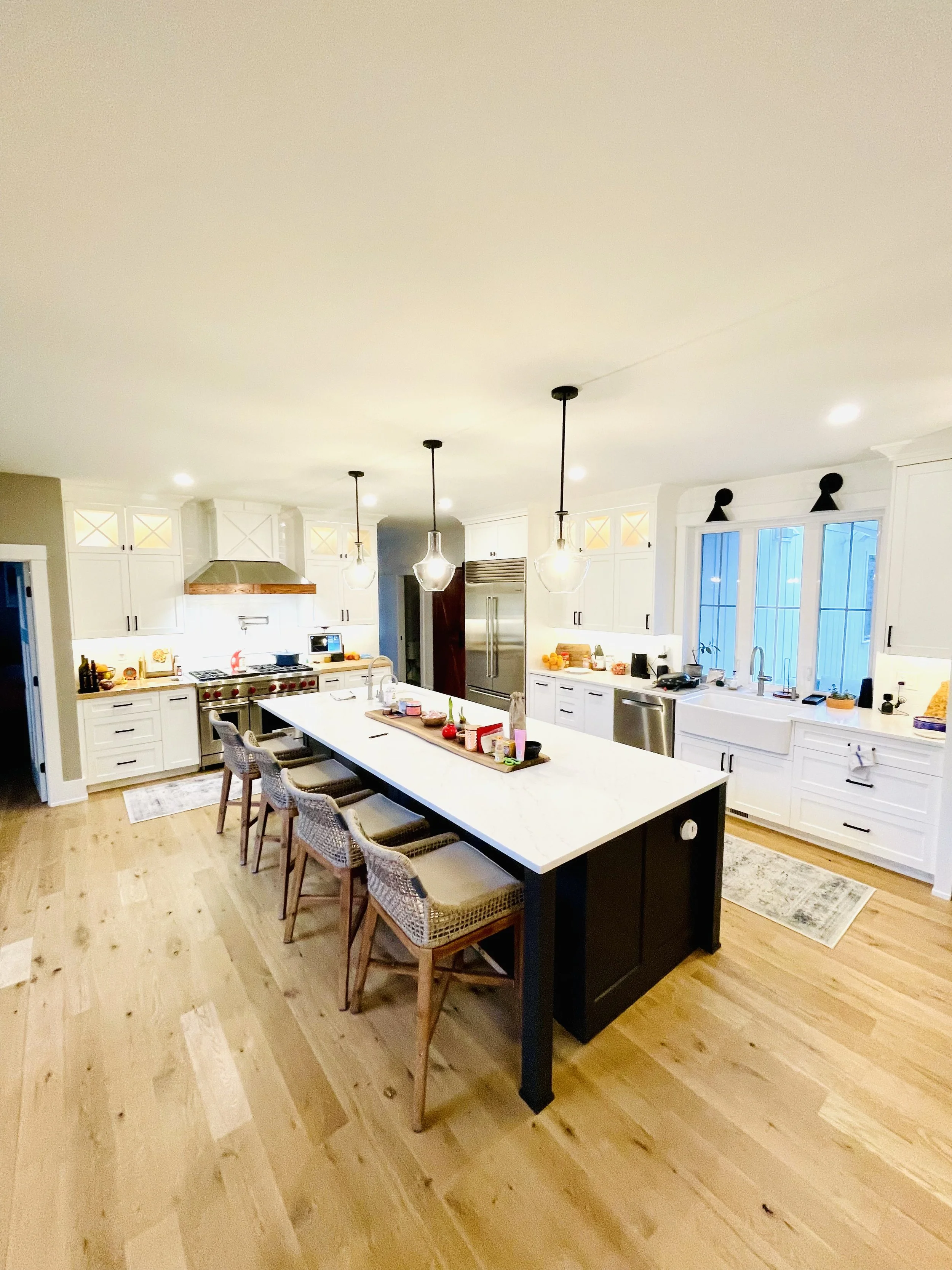 Modern kitchen with white cabinets, a large island with a white countertop, four pendant lights, stainless steel appliances, and hardwood floors.