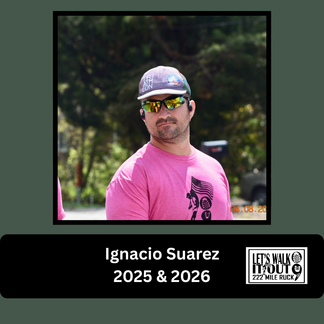 A man in a pink shirt with a graphic of a person walking with a flag, wearing sunglasses, a cap, and earbuds, outdoors with trees in the background.