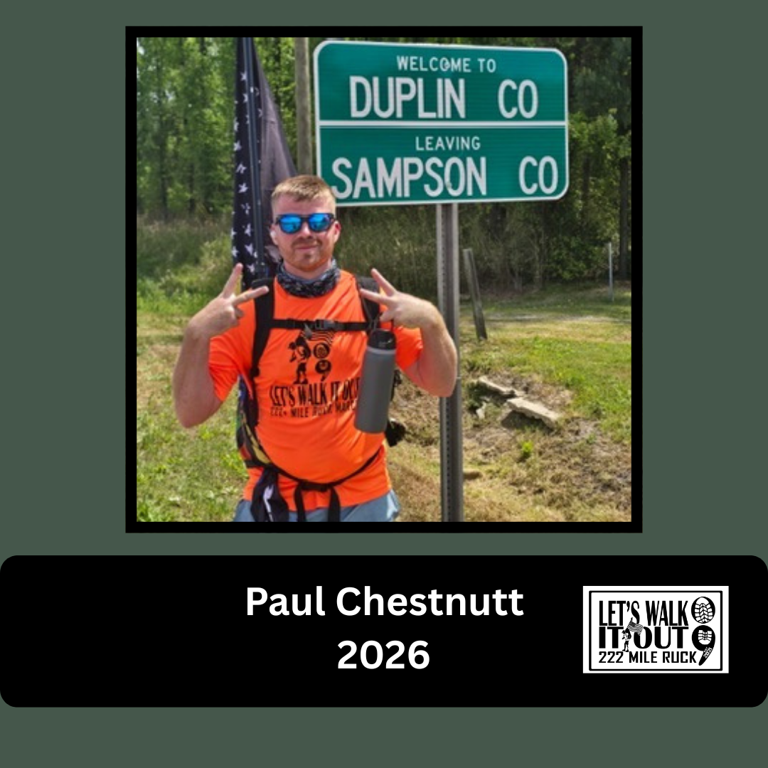 Person standing outdoors near a green sign that reads 'Welcome to Duplin Co, Leaving Sampson Co.' Wearing sunglasses, an orange shirt, and a backpack, making peace signs with both hands.