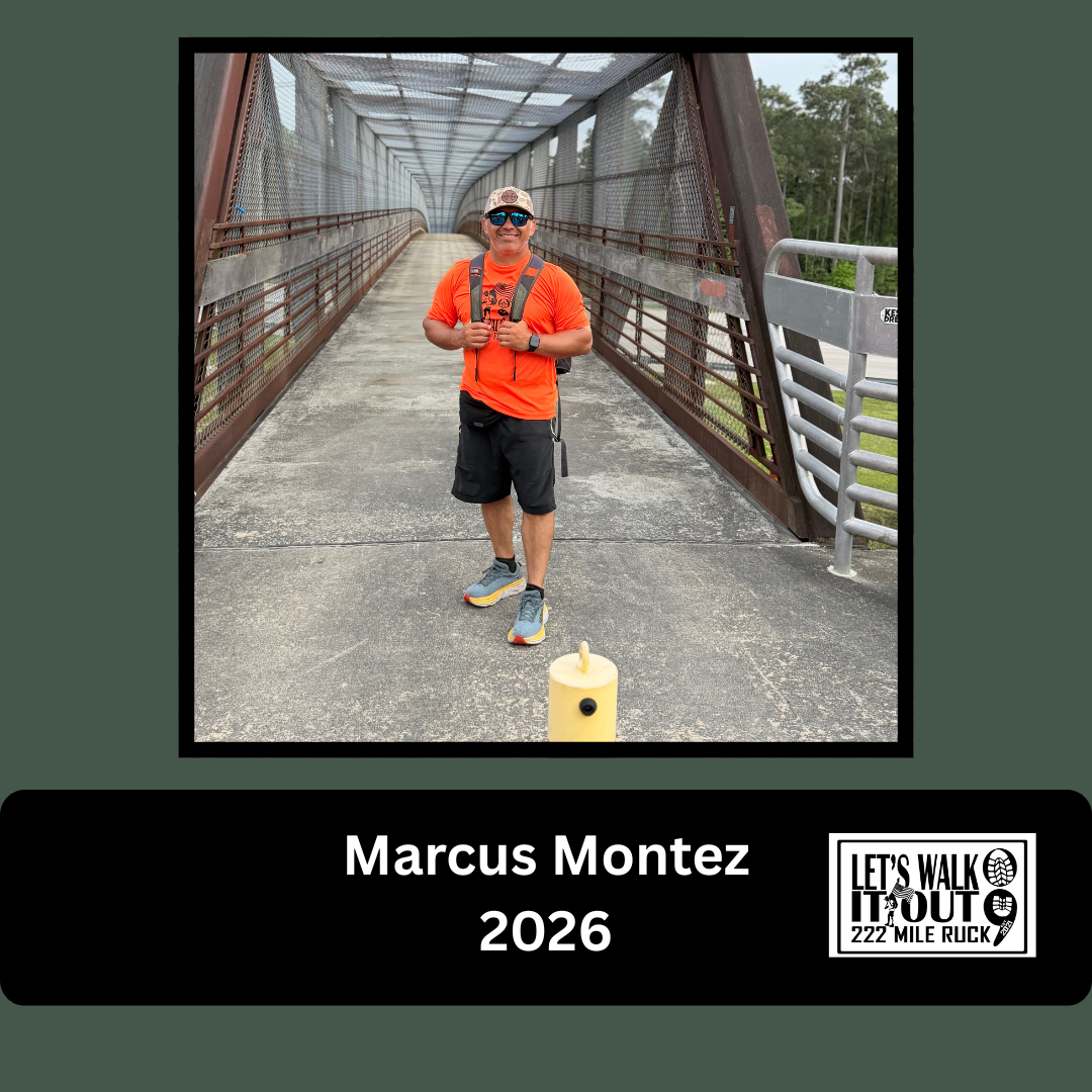 A man standing on a pedestrian bridge with a metal mesh roof, wearing a bright orange shirt, black shorts, and sunglasses. He has a backpack, a hat, and a smartwatch, and is smiling at the camera. There is a yellow post in front of him. The photo is 