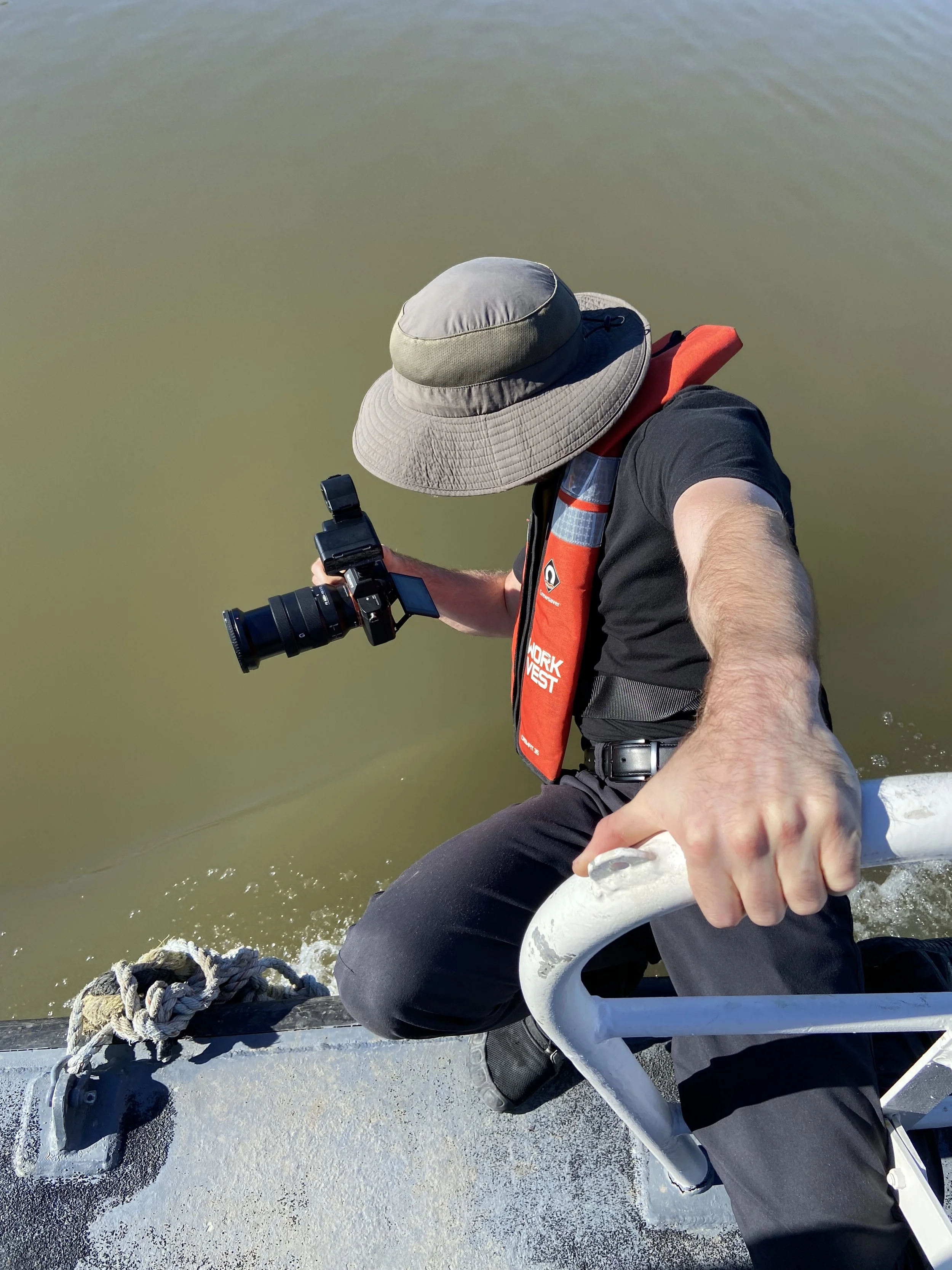 Person wearing a sun hat and life vest taking a photo from a boat.