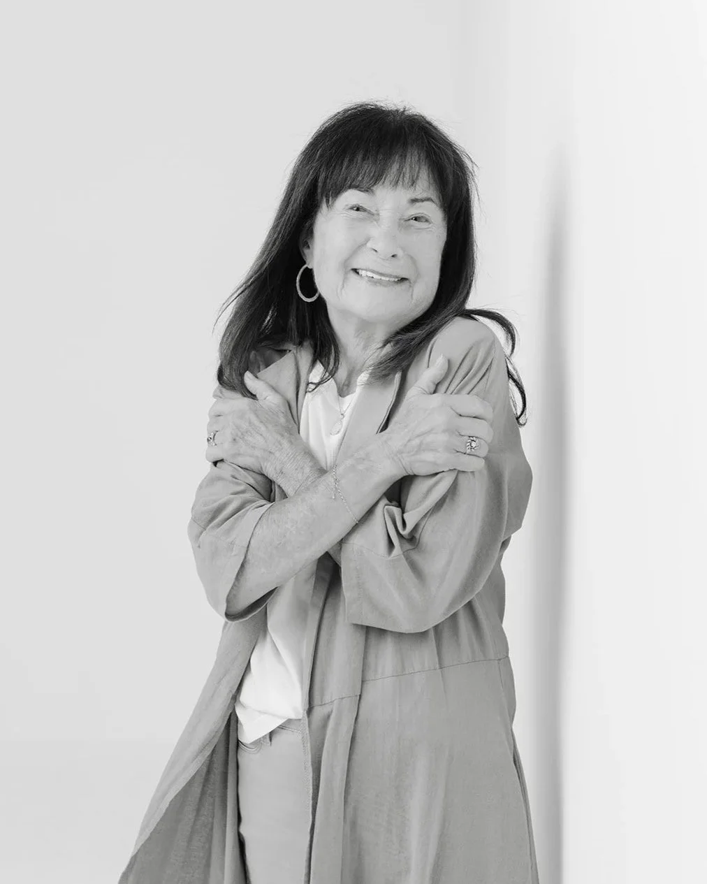 Black and white portrait of Jackie Cole smiling and leaning against a studio wall during her 50 Women Project photoshoot with Christine Harris.