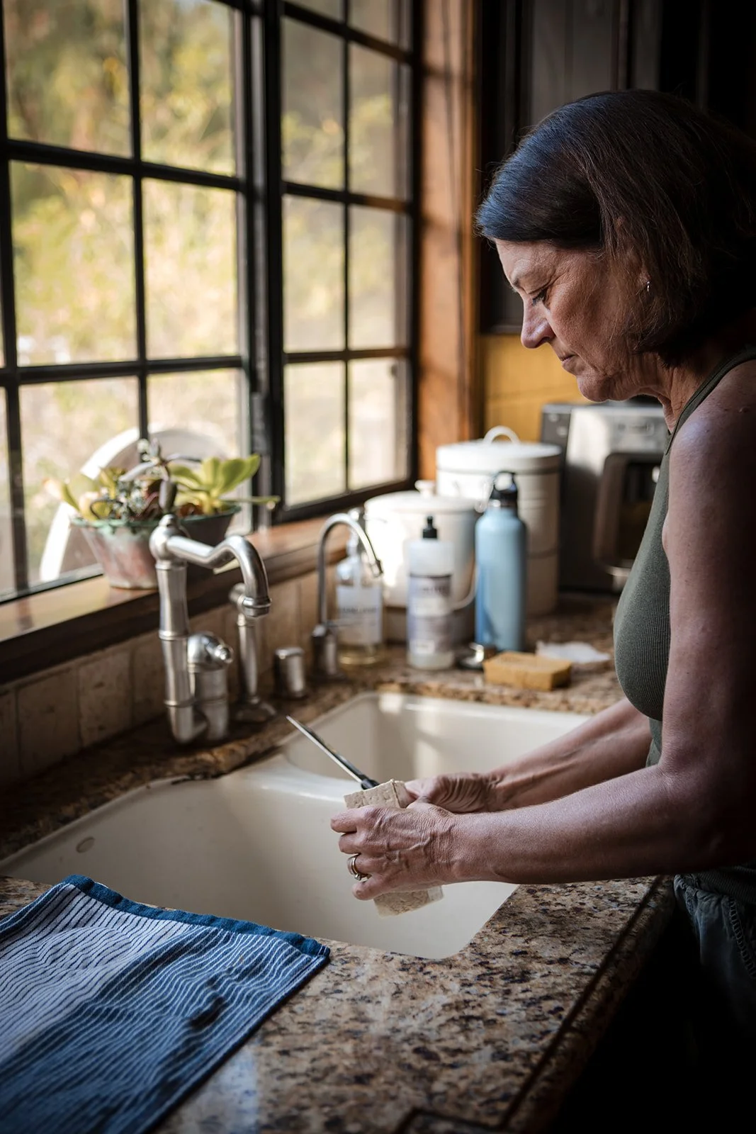 Paula Hodgson at the kitchen sink, morning light, photographed by Christine Harris