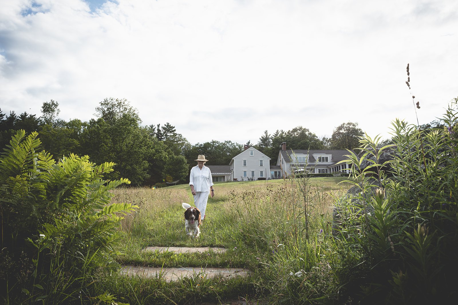 Jeanne Henriques walking along the garden path at Tahilla Farm in Peterborough, New Hampshire, with her dog Tawni on a summer afternoon