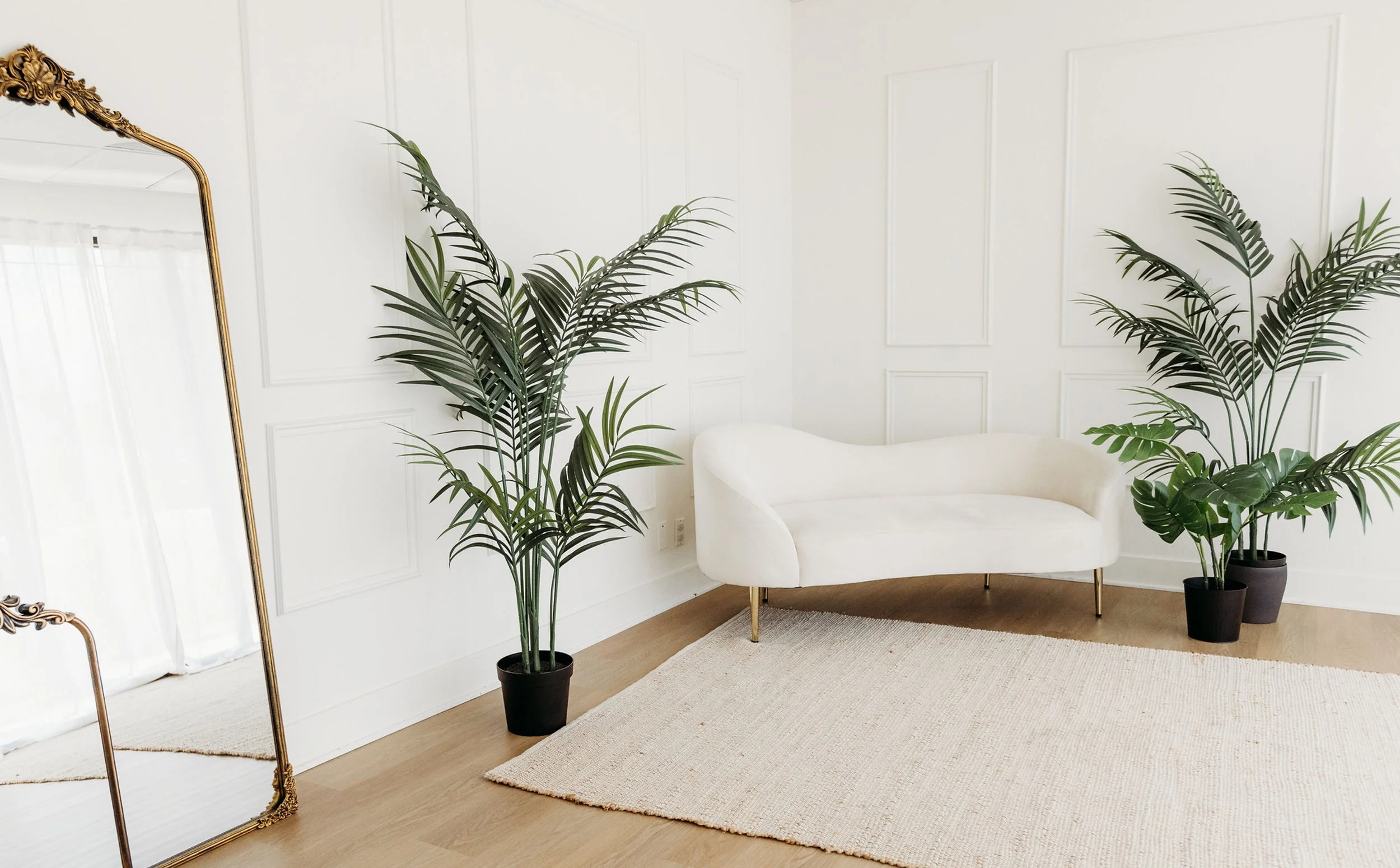 Natural light room at The Arlen Studio in Westlake Village, California, featuring white walls, a cream settee, palm plants, and a ornate gold floor mirror. Photography by Christine Harris.