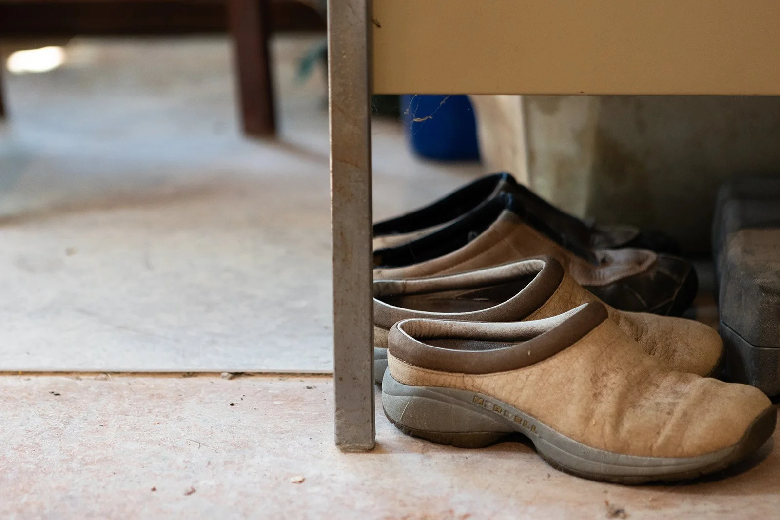 A pair of well-worn clogs tucked beneath a studio shelf, a quiet detail from ceramist Sunny Leinhart's workspace.