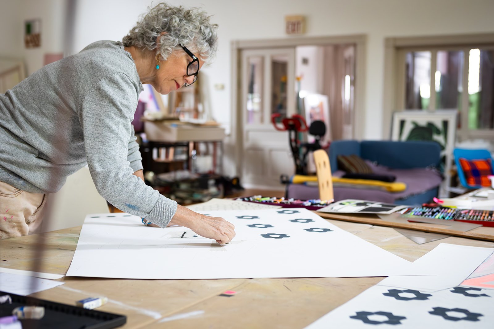 Artist Michelle Weinberg leans over her worktable arranging a piece in her Sharon Springs studio, photographed by Christine Harris.
