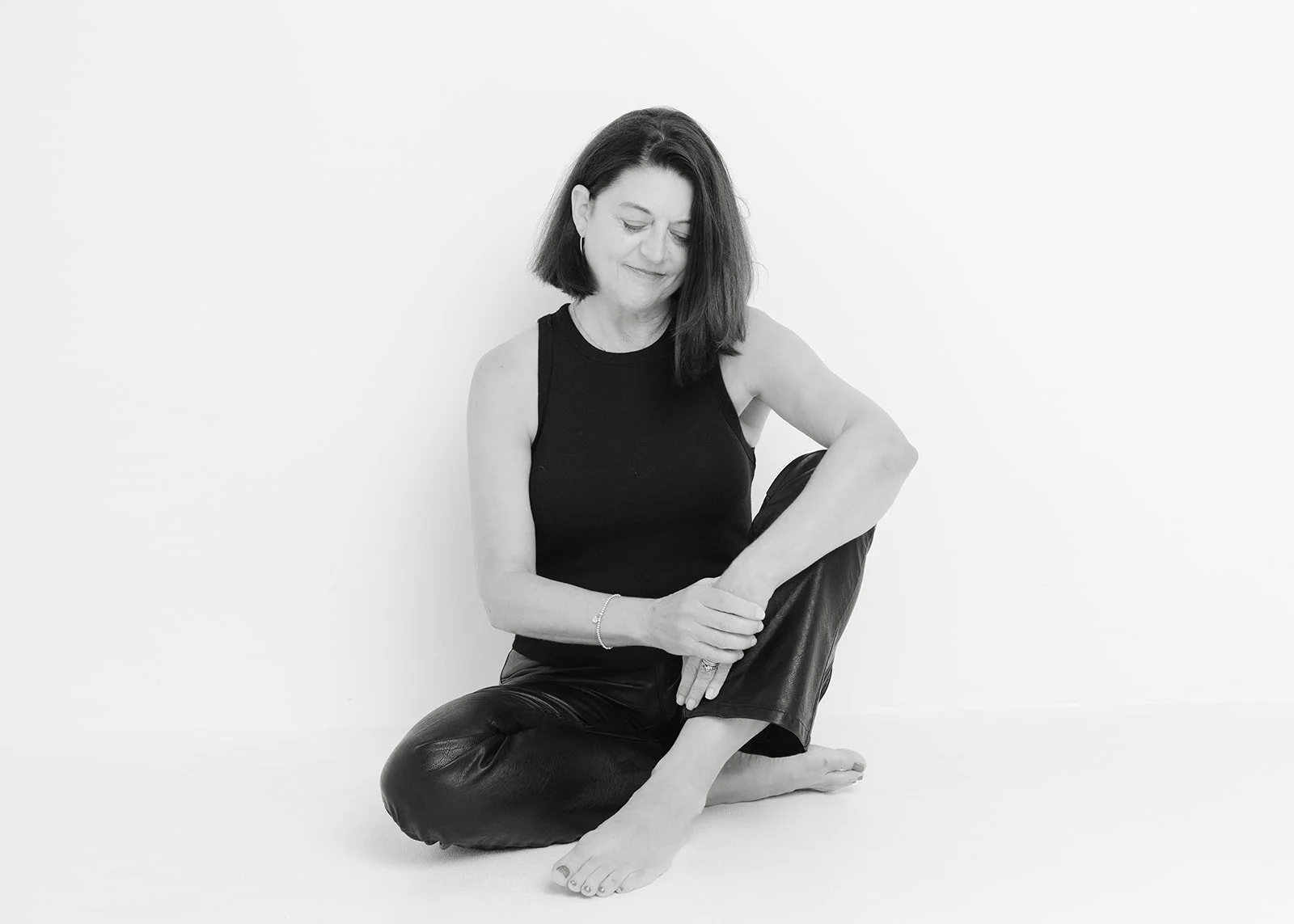 Black and white portrait of Paula Hodgson seated barefoot on the studio floor during her 50 Women Project portrait session with photographer Christine Harris.