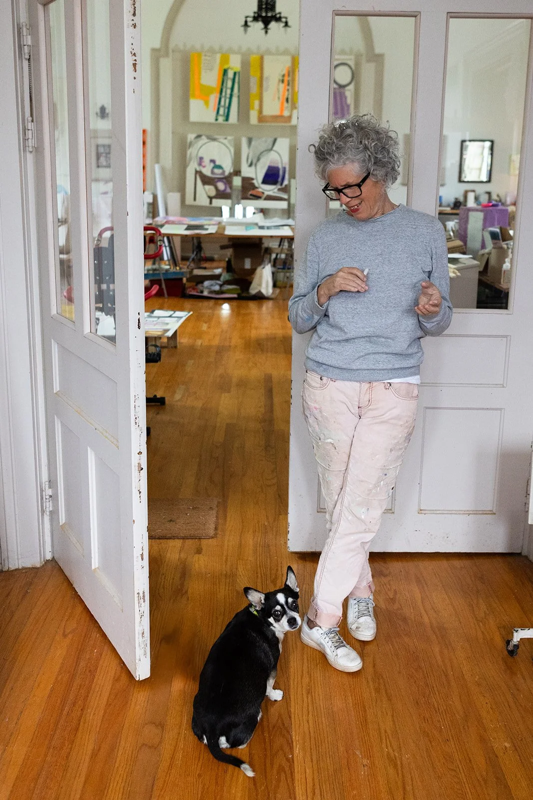 Artist Michelle Weinberg stands in her studio doorway sharing a moment with her dog, photographed by Christine Harris.