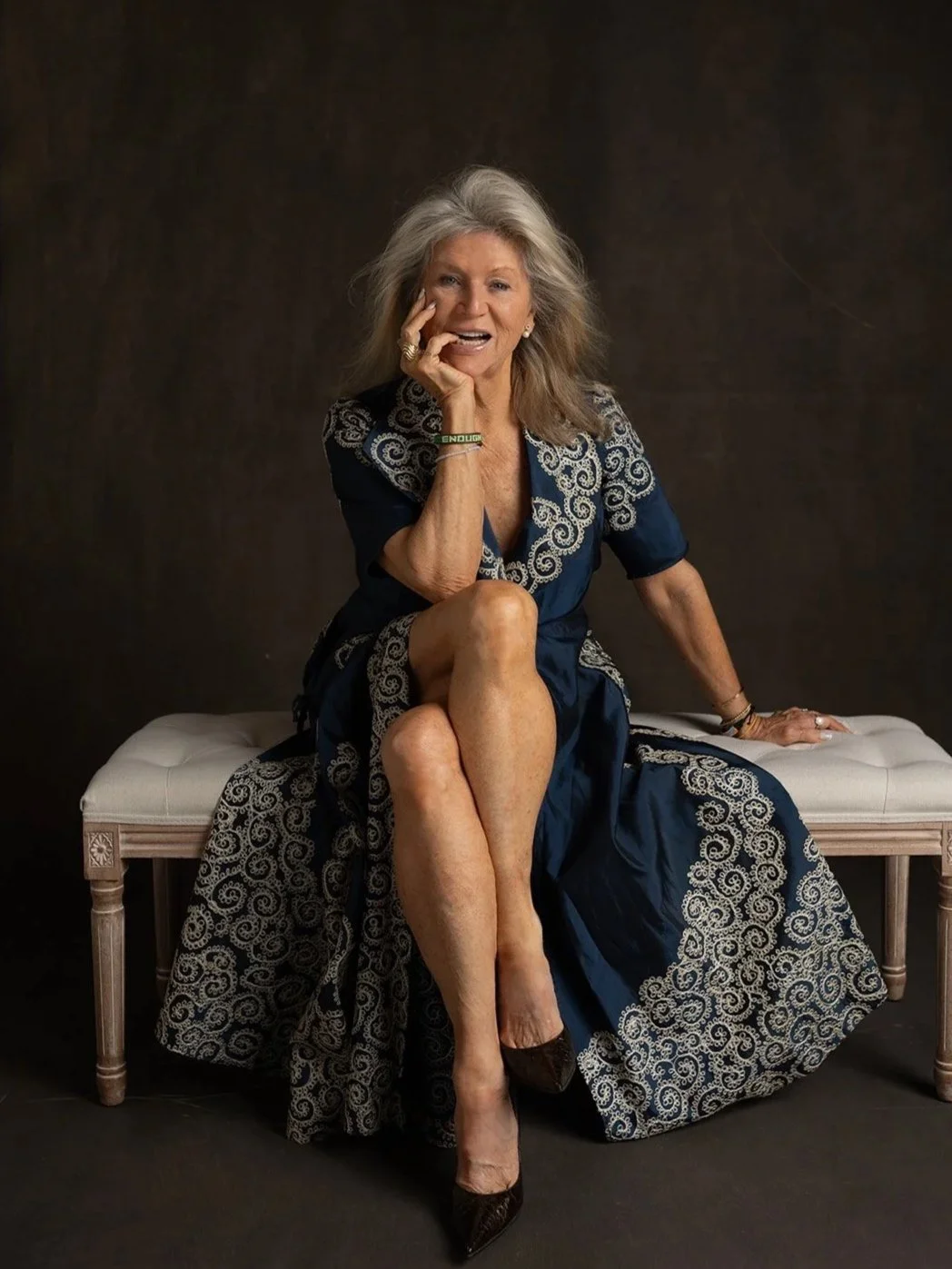 Leigh Kilton-Smith smiles while seated on a vintage bench in a blue embroidered dress during her 50 Women Project portrait session by Christine Harris.