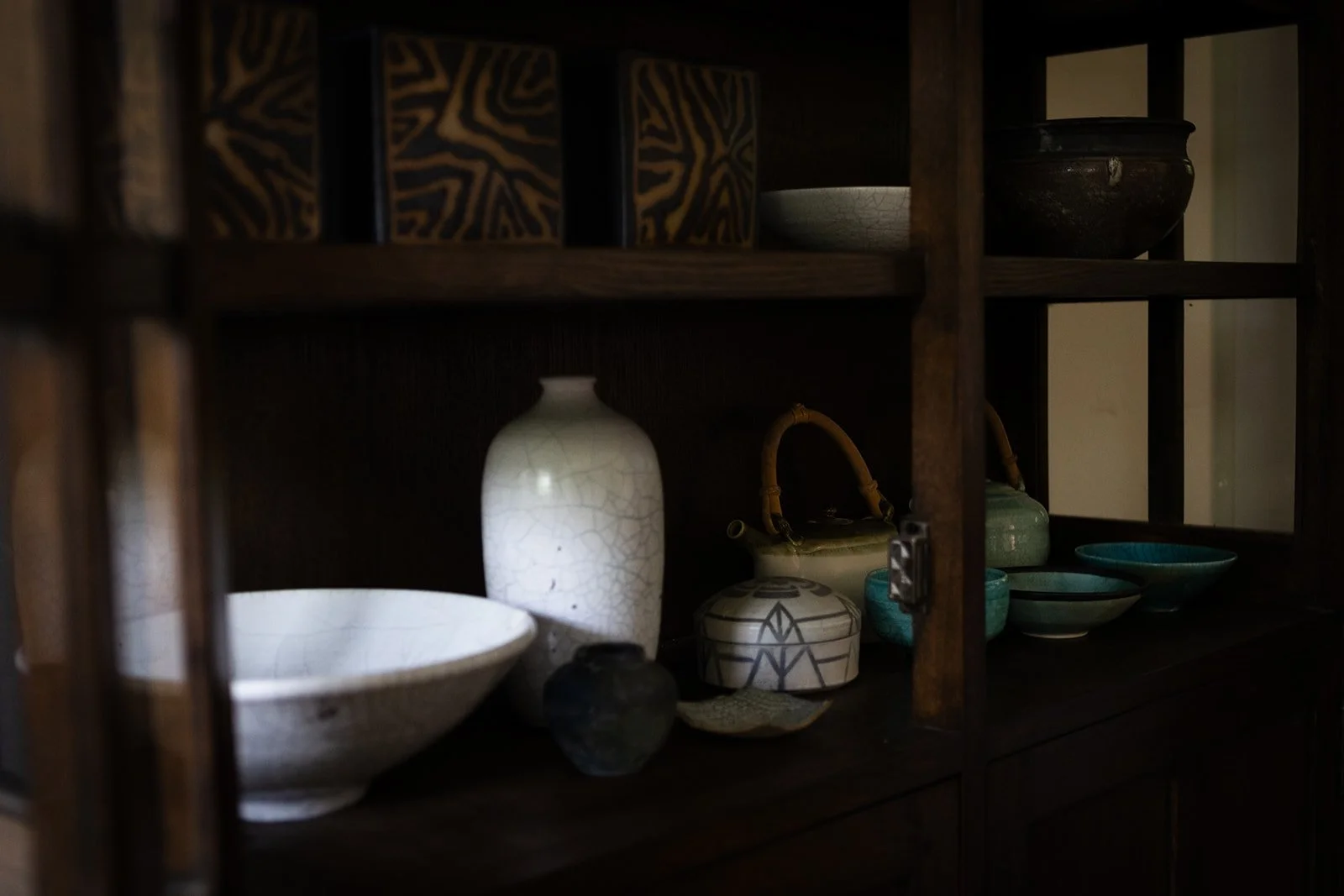 A dark wood shelf holds a collection of Sunny Leinhart's ceramic vessels, bowls, and a teapot in her studio.